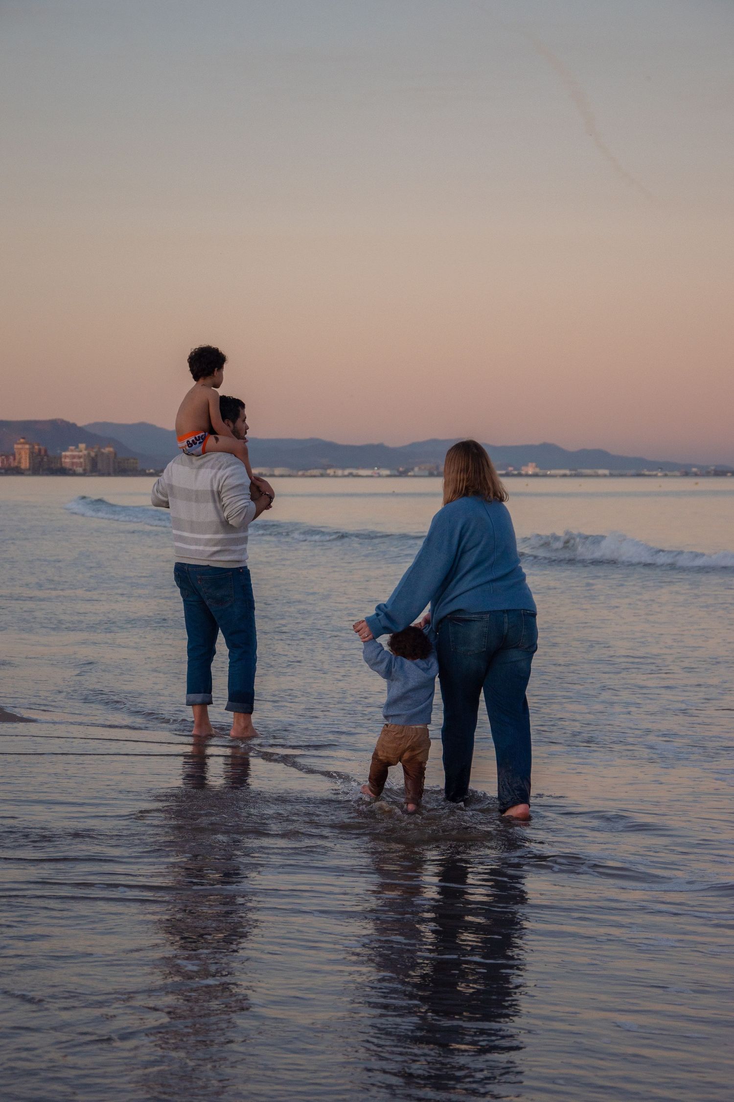 Small group wades in ocean water during sunset with mountains visible in distance.