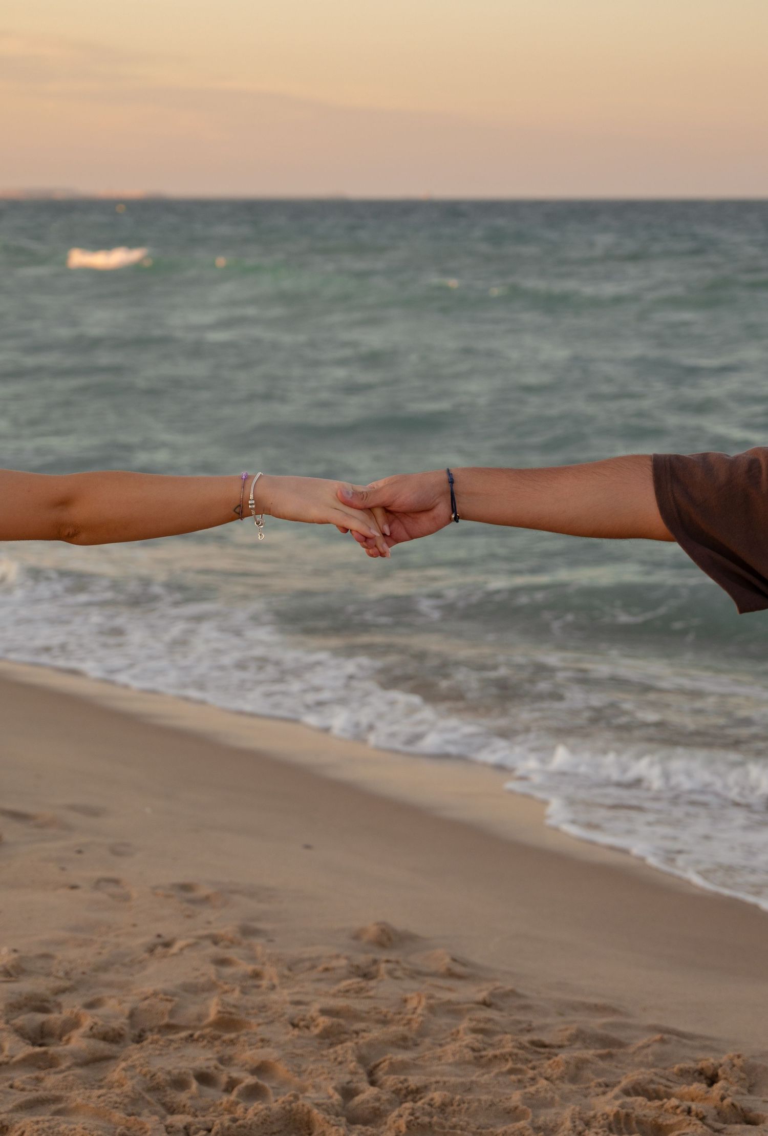 Two hands reaching to connect against a beach sunset backdrop.