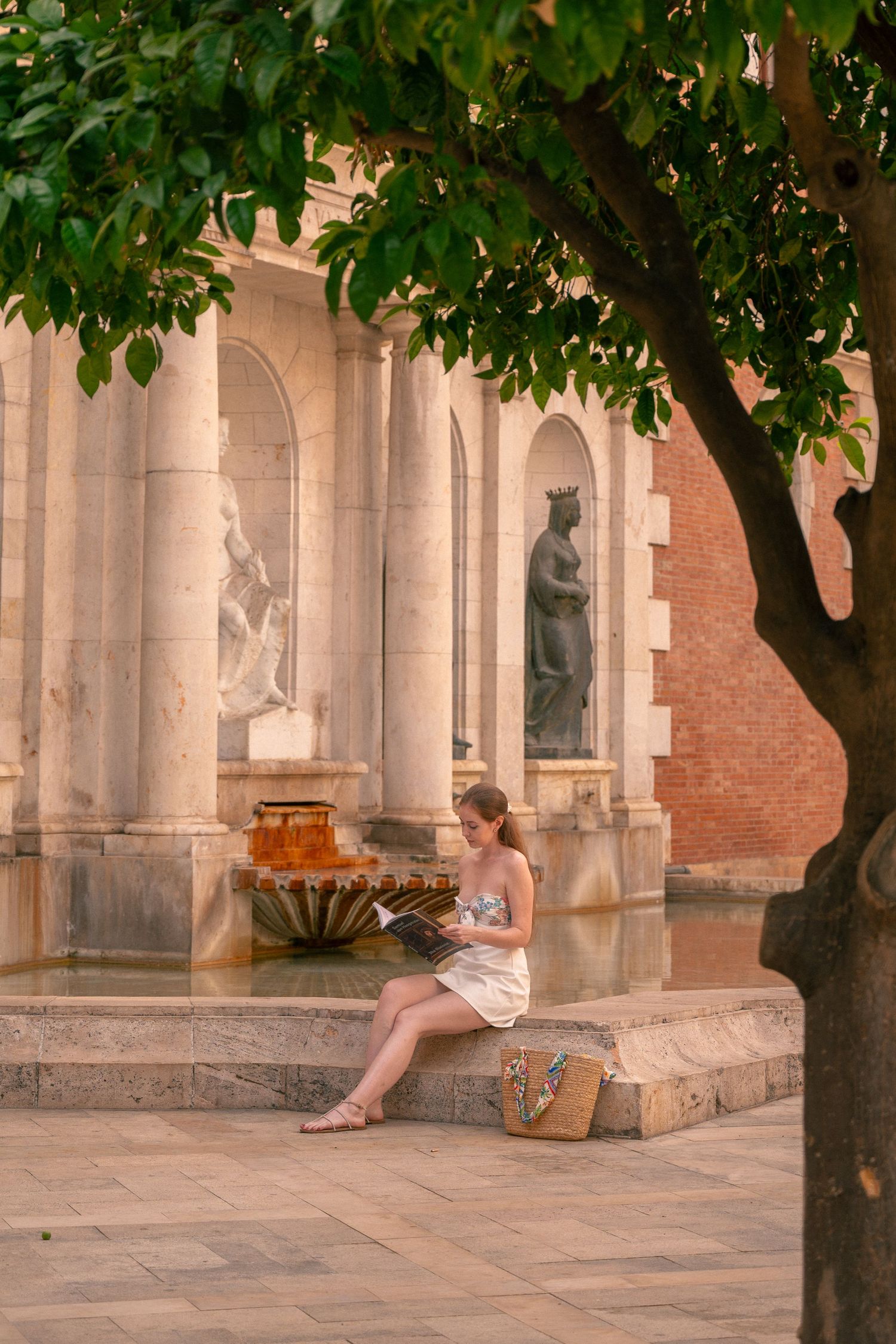Person sitting on steps of historic building with columns and trees.
