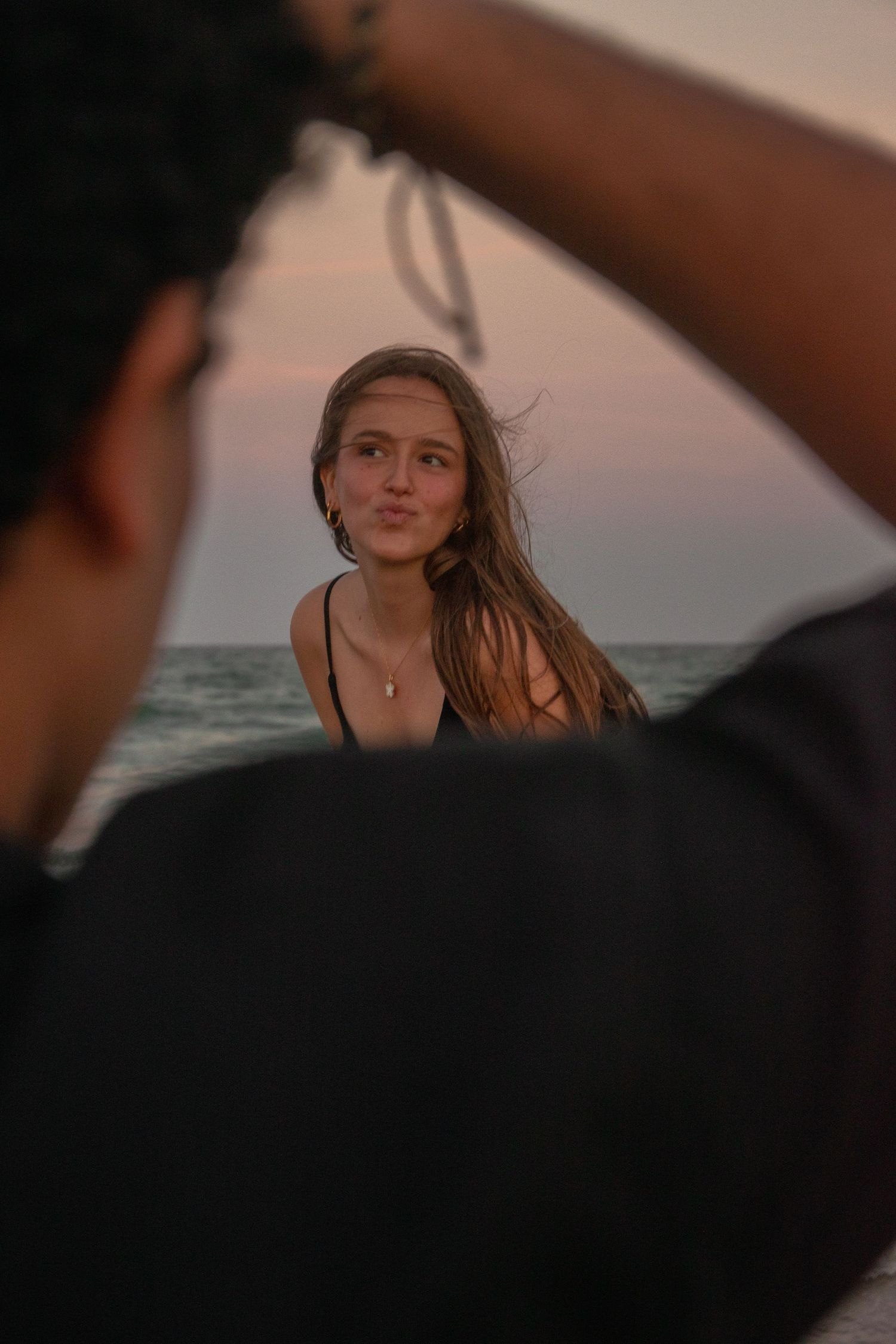 Person with windswept hair poses on beach during sunset.