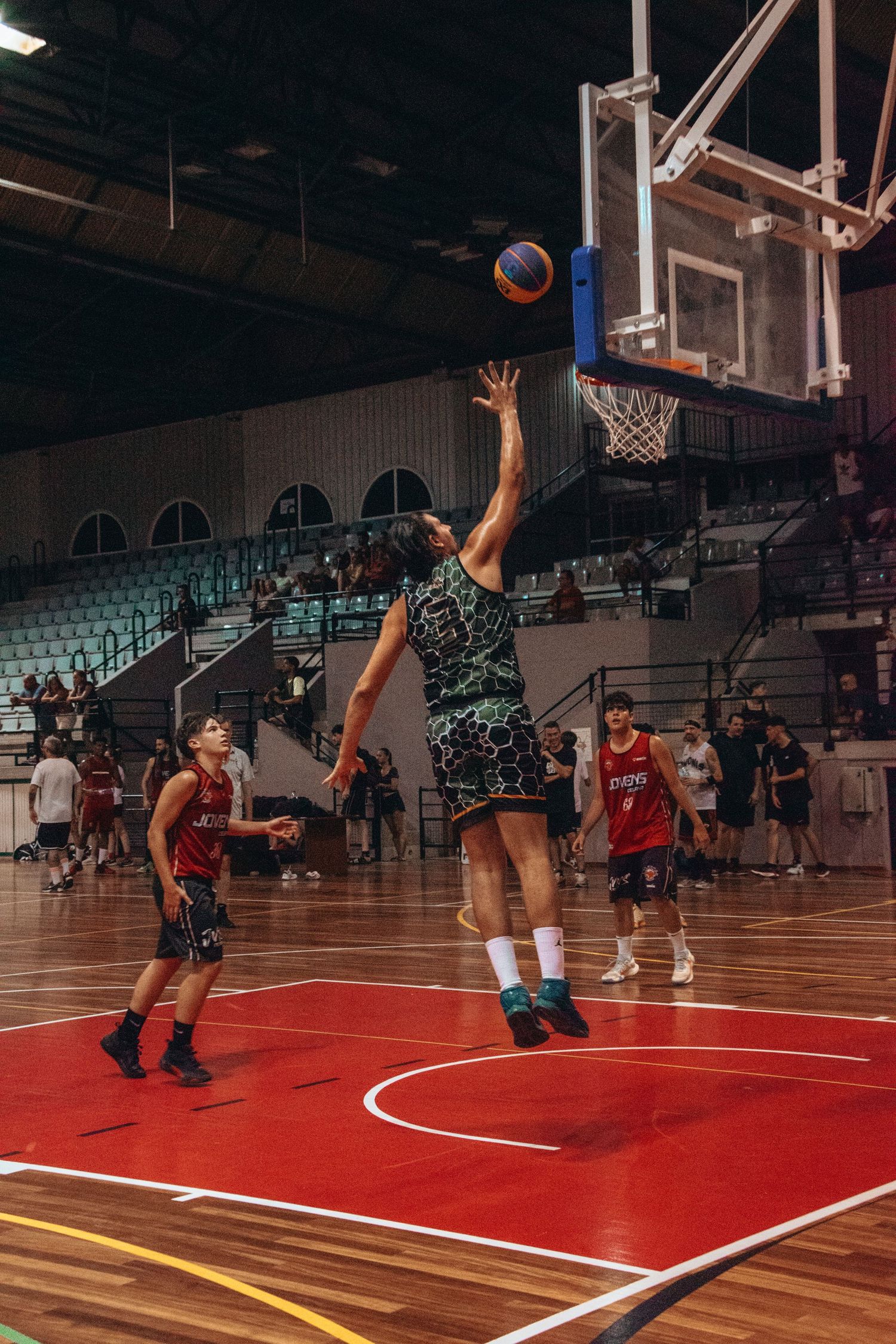 Players competing for a rebound on a red and wooden basketball court.