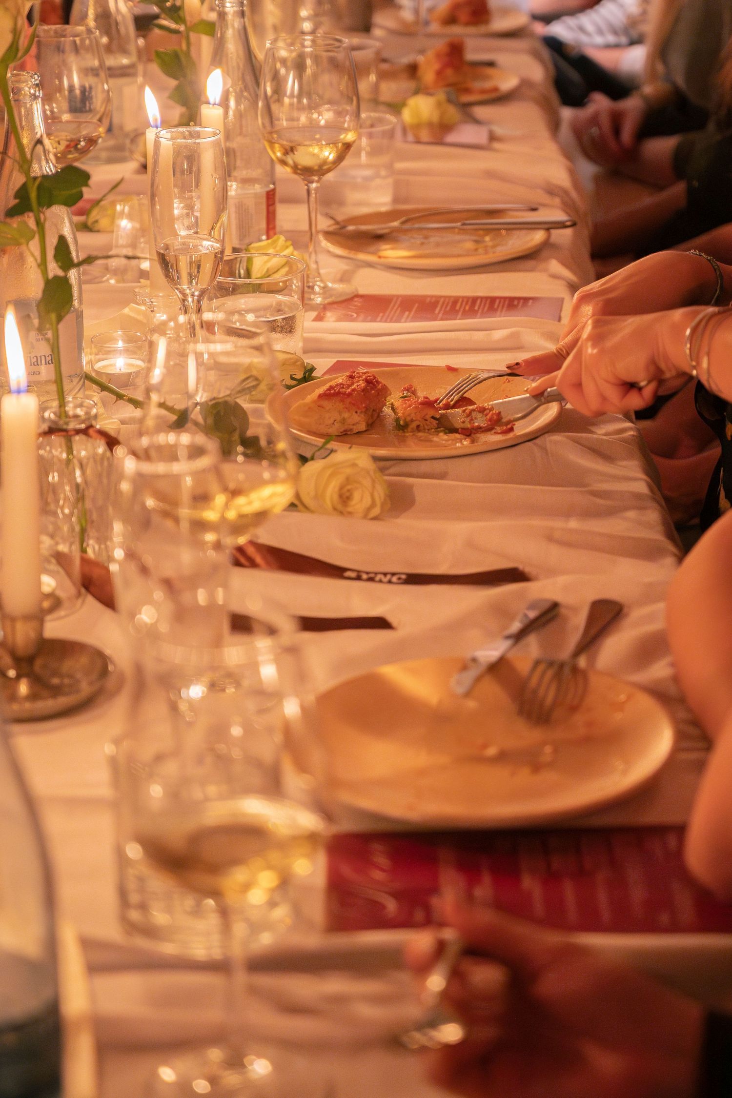 An elegant dinner table setting with wine glasses, candles, and place settings in warm ambient lighting.