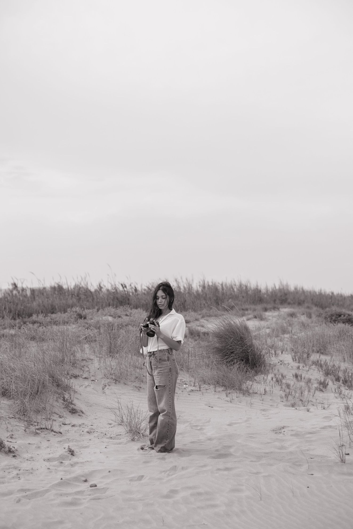 Photographer lying on sandy beach dunes taking artistic shots with professional camera equipment.
