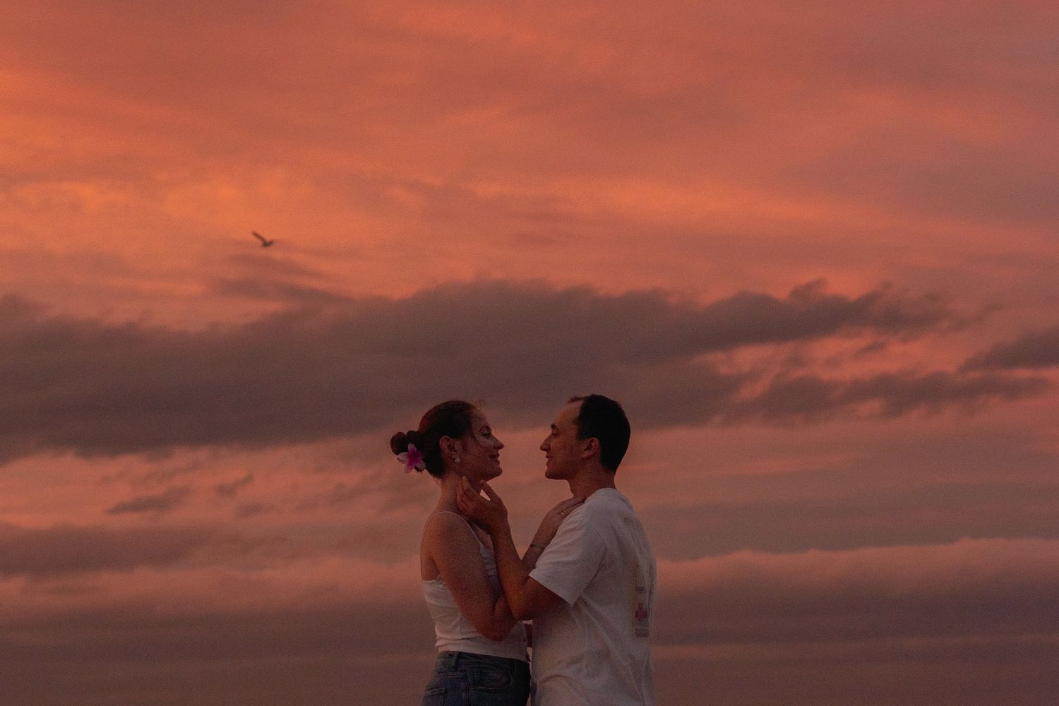Silhouetted couple embracing against dramatic orange sunset sky.