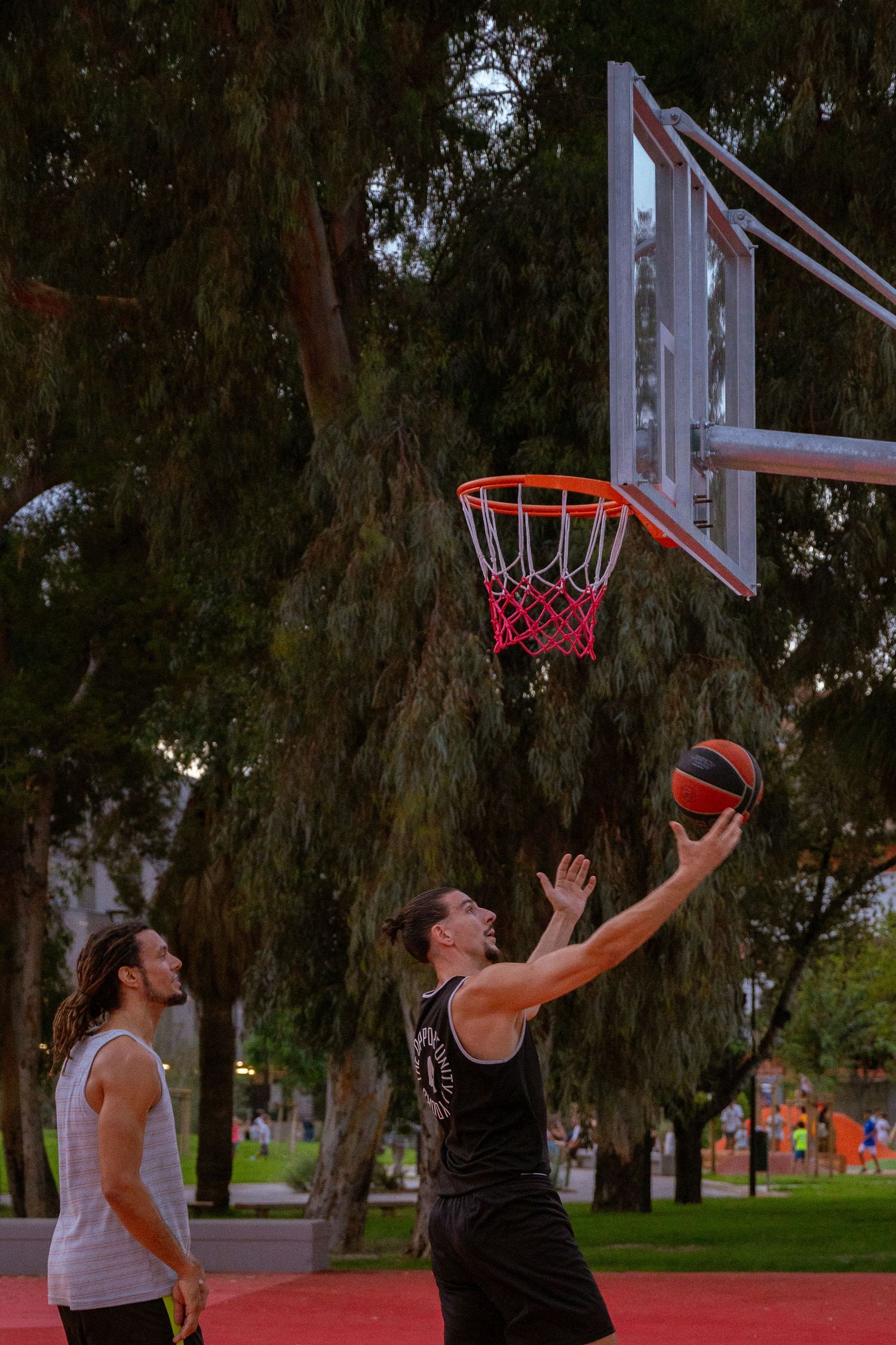 Basketball players jumping for shots at outdoor court with trees in background.