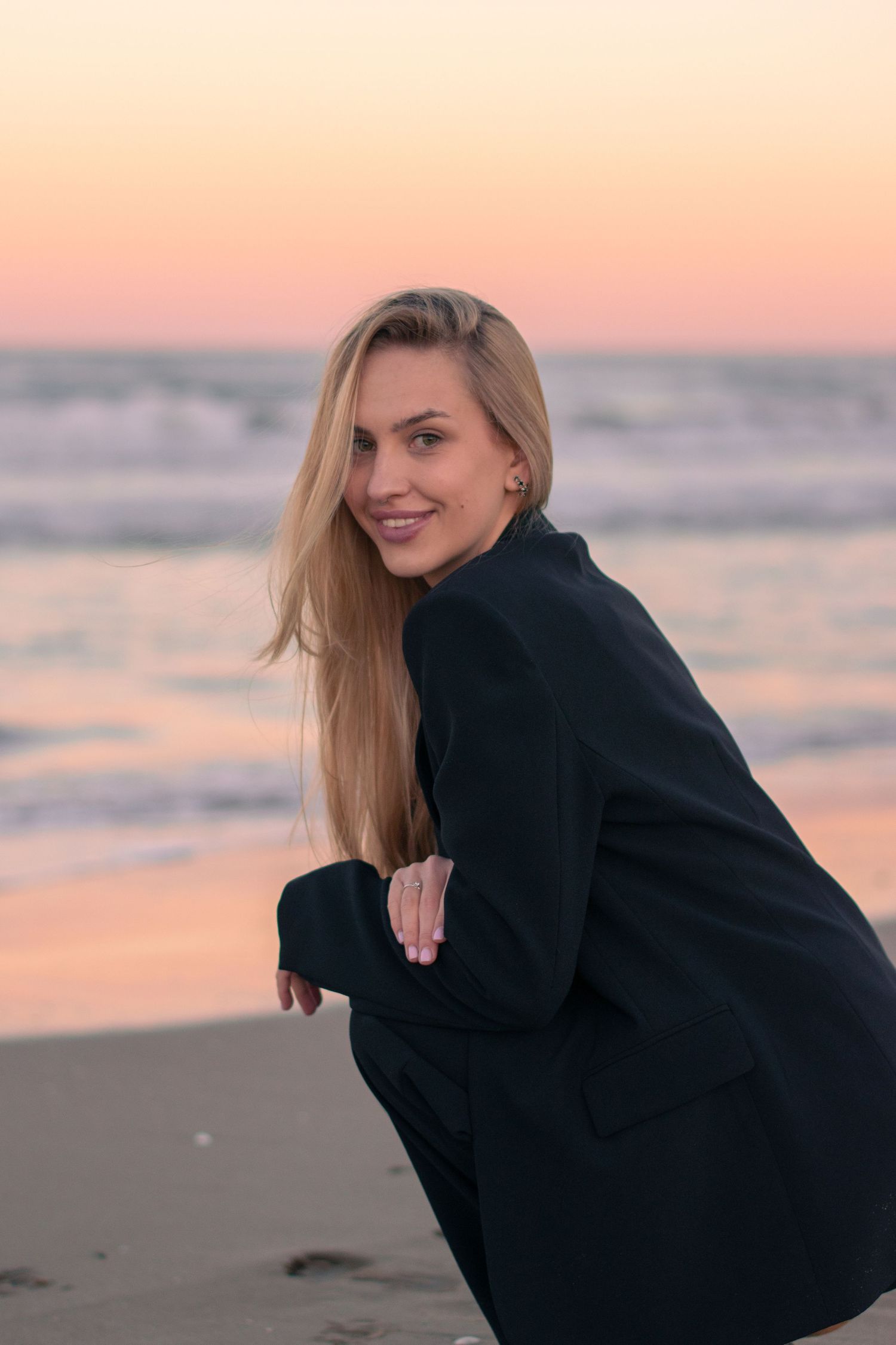 A figure in dark clothing poses on sandy beach during sunset.