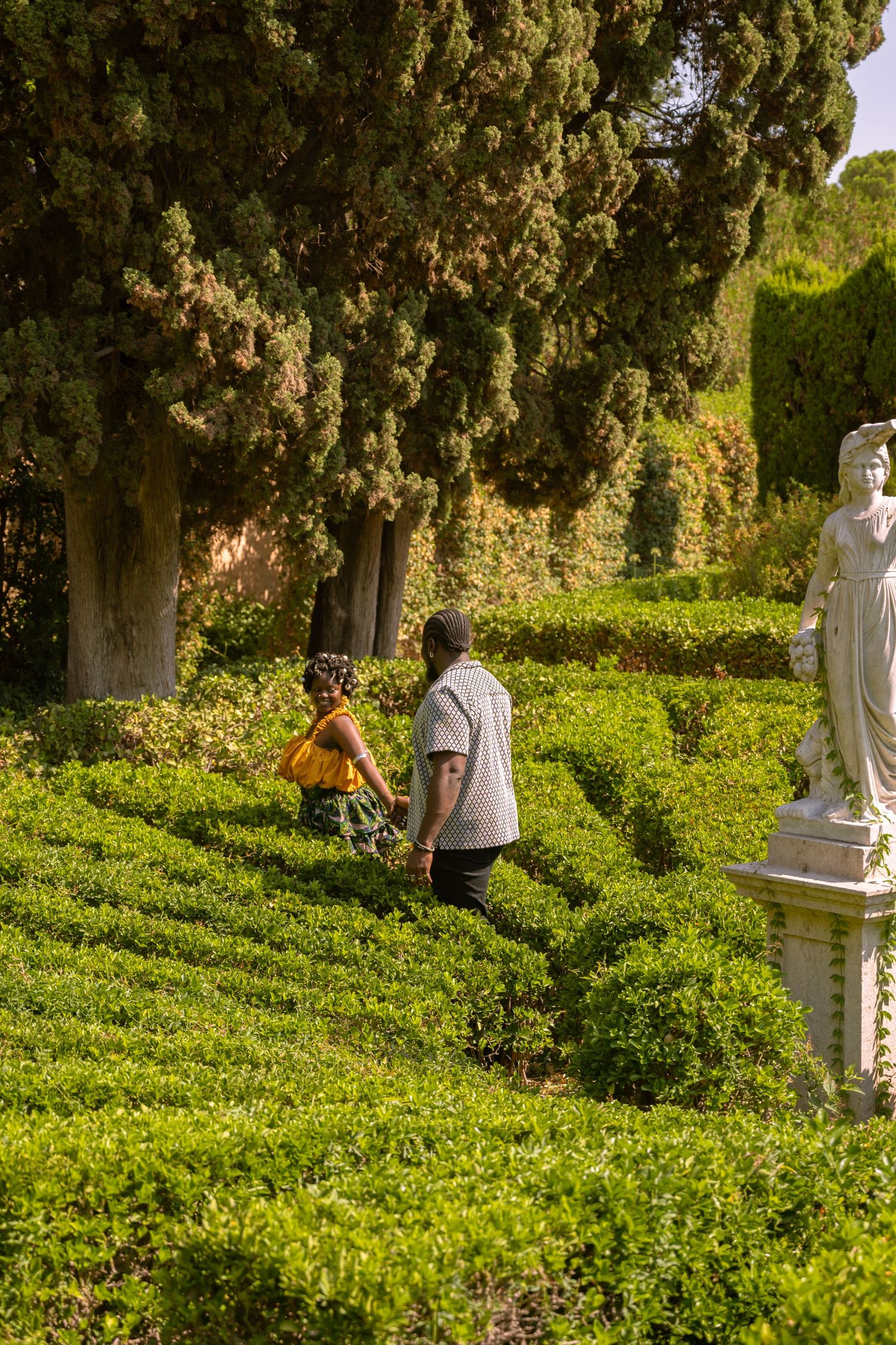 Group walking through a verdant garden path with tall cypress trees.