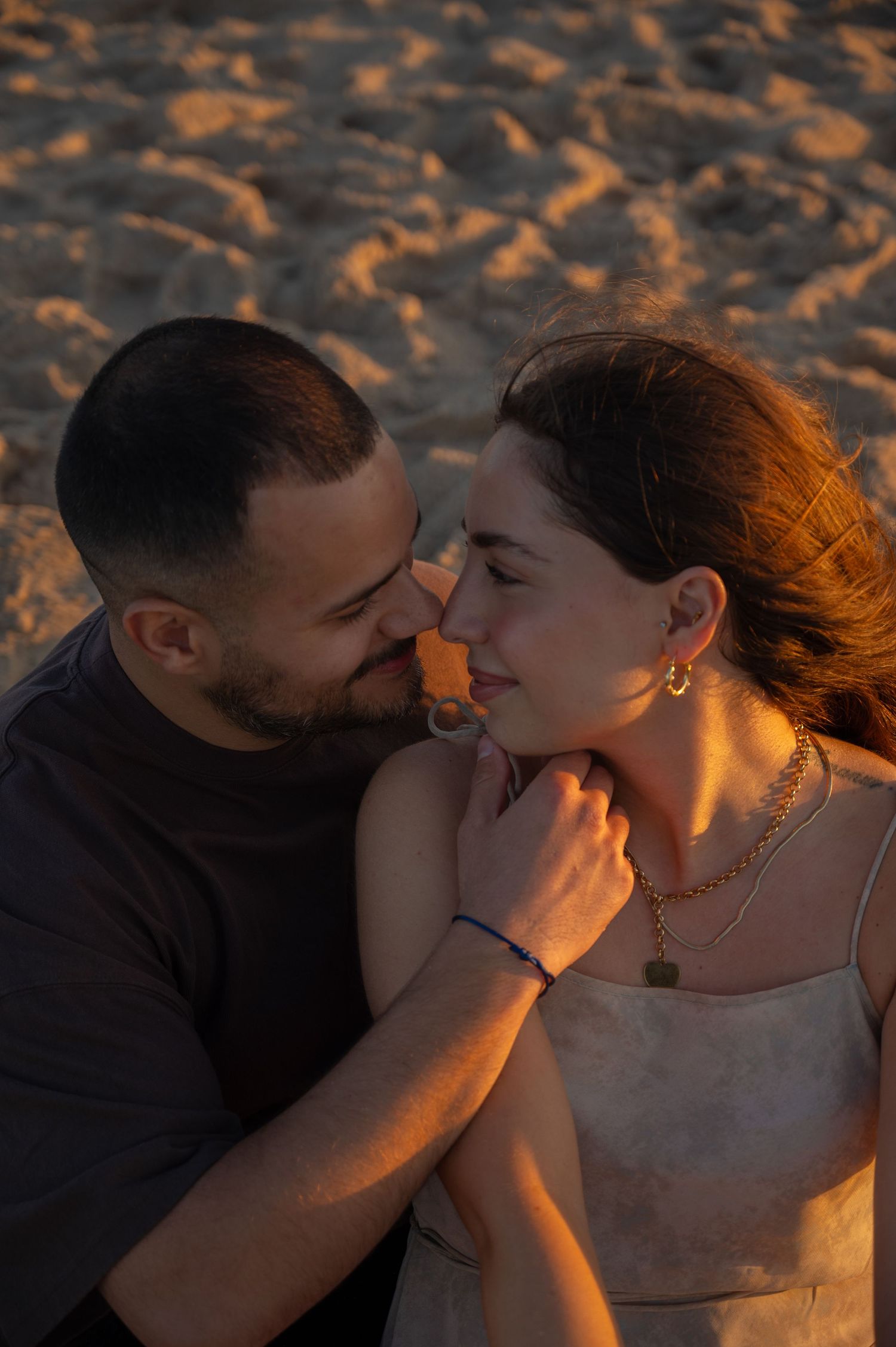 A romantic couple shares intimate kisses on the beach during golden hour sunset.