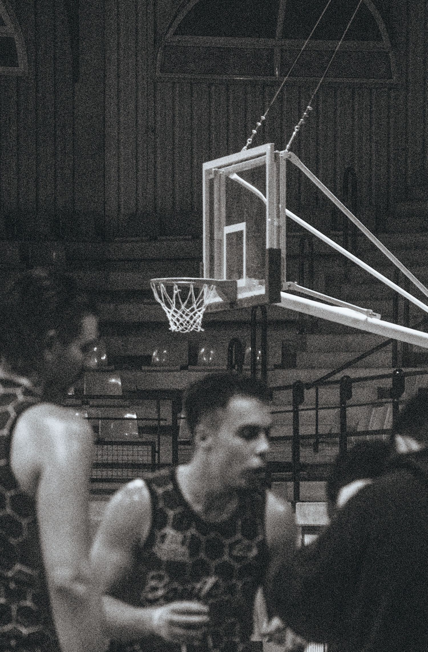 Indoor basketball court with players and equipment visible in low light conditions.