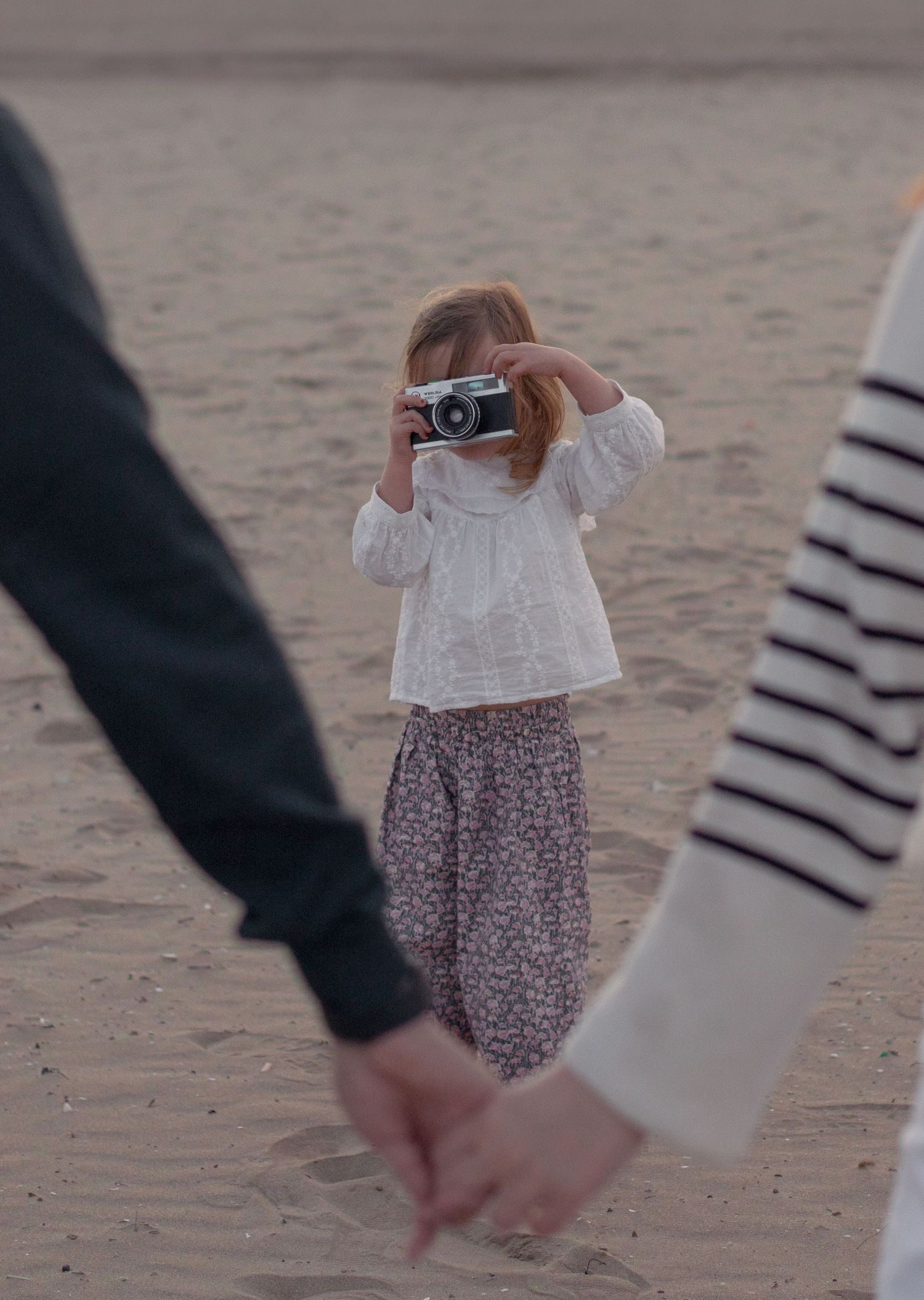 People holding hands while walking on beach at sunset.