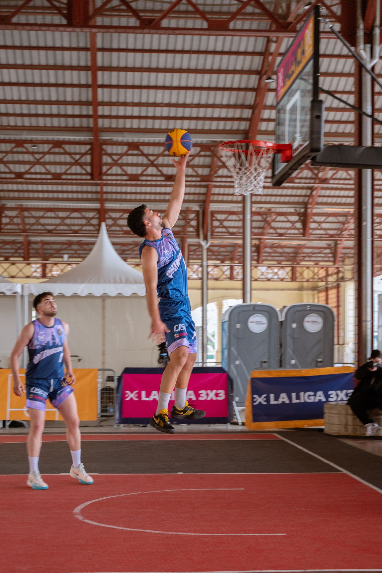 Player jumping high to make a shot during an outdoor basketball game.