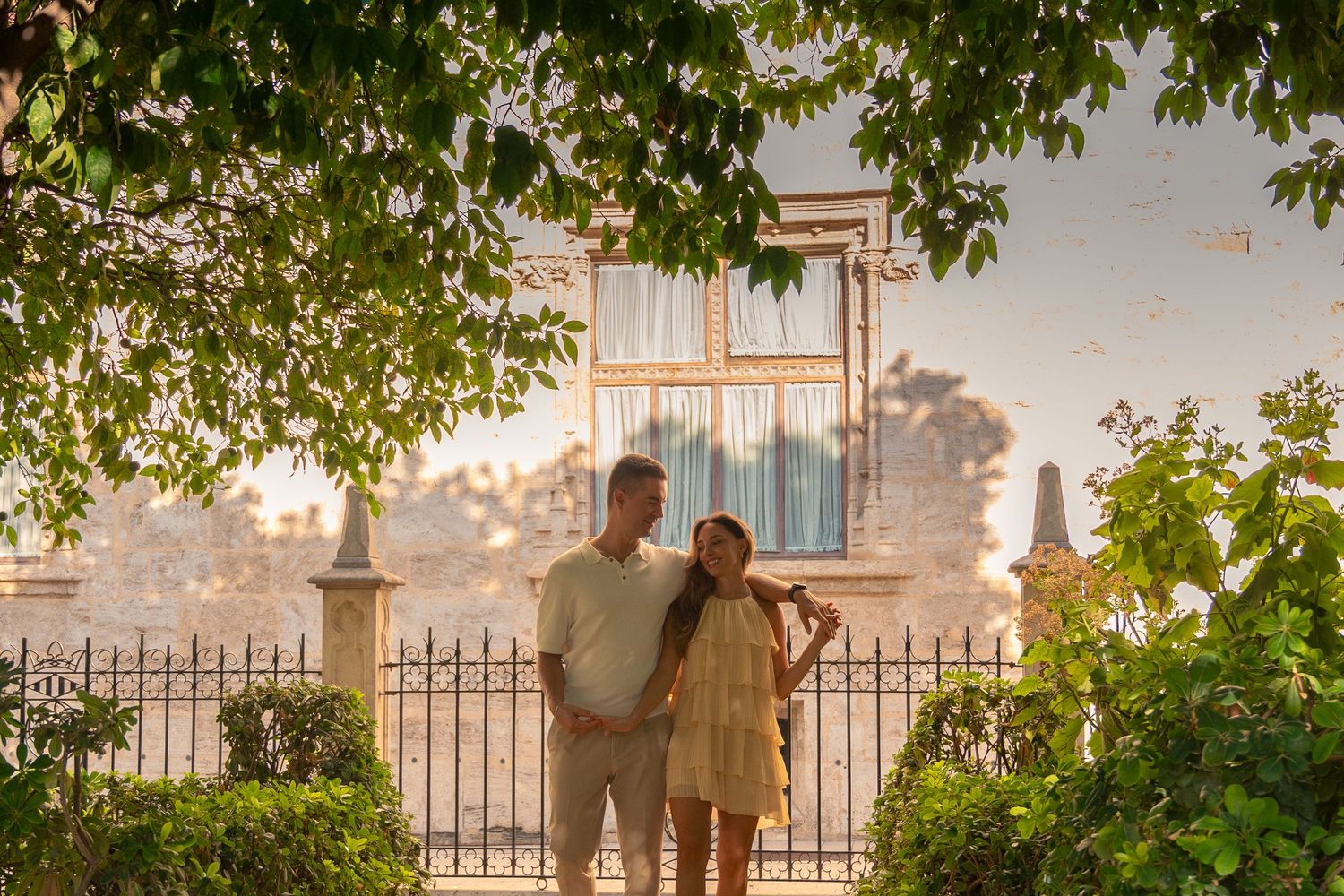 A couple standing in front of a building during golden hour with tree branches framing the scene.