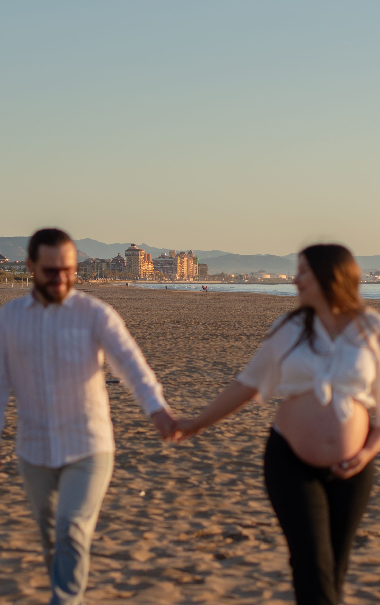 People in white clothing dance playfully together on sandy beach at dusk.