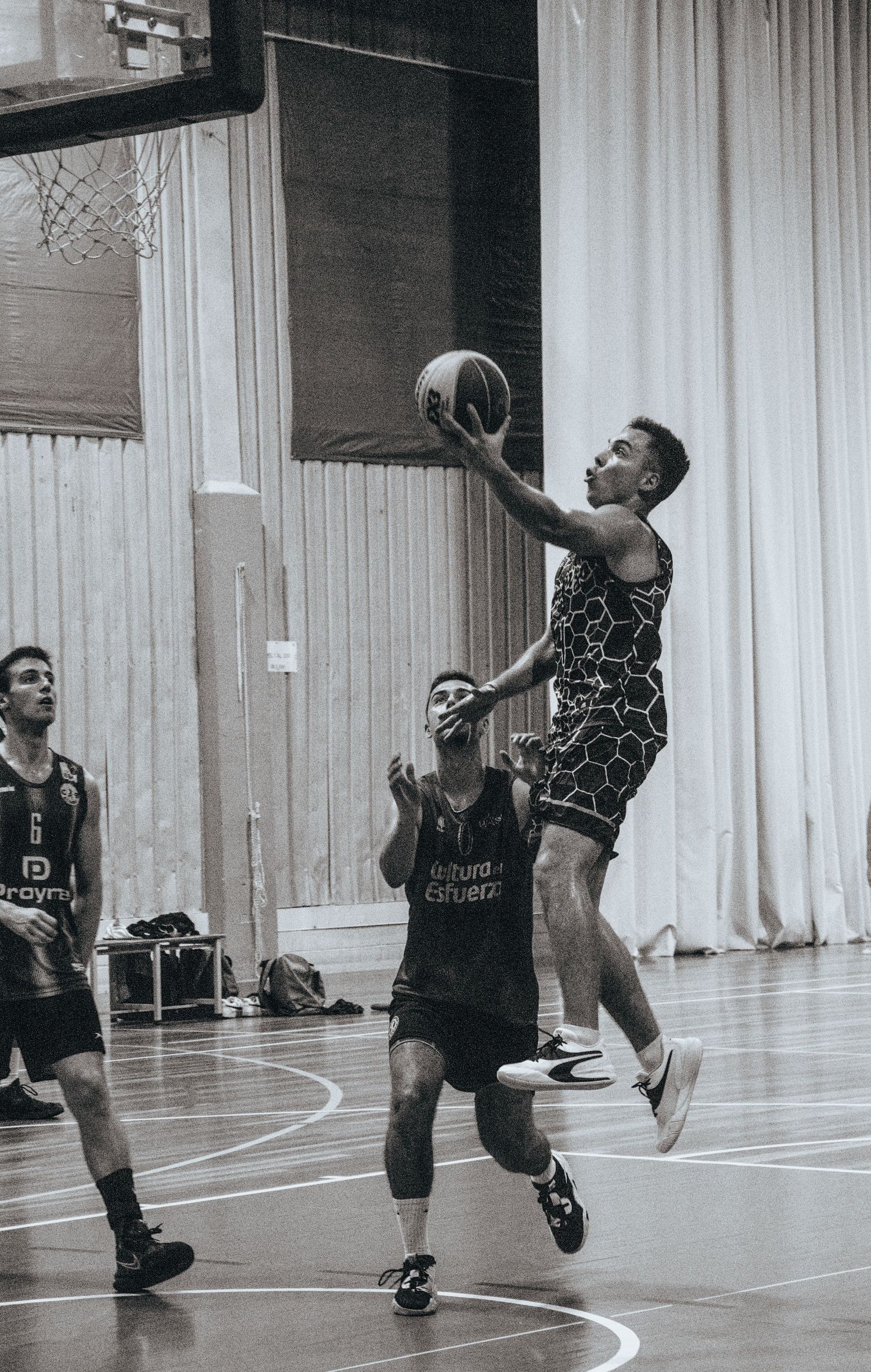 Basketball player leaping for a layup during an indoor game with defenders nearby.