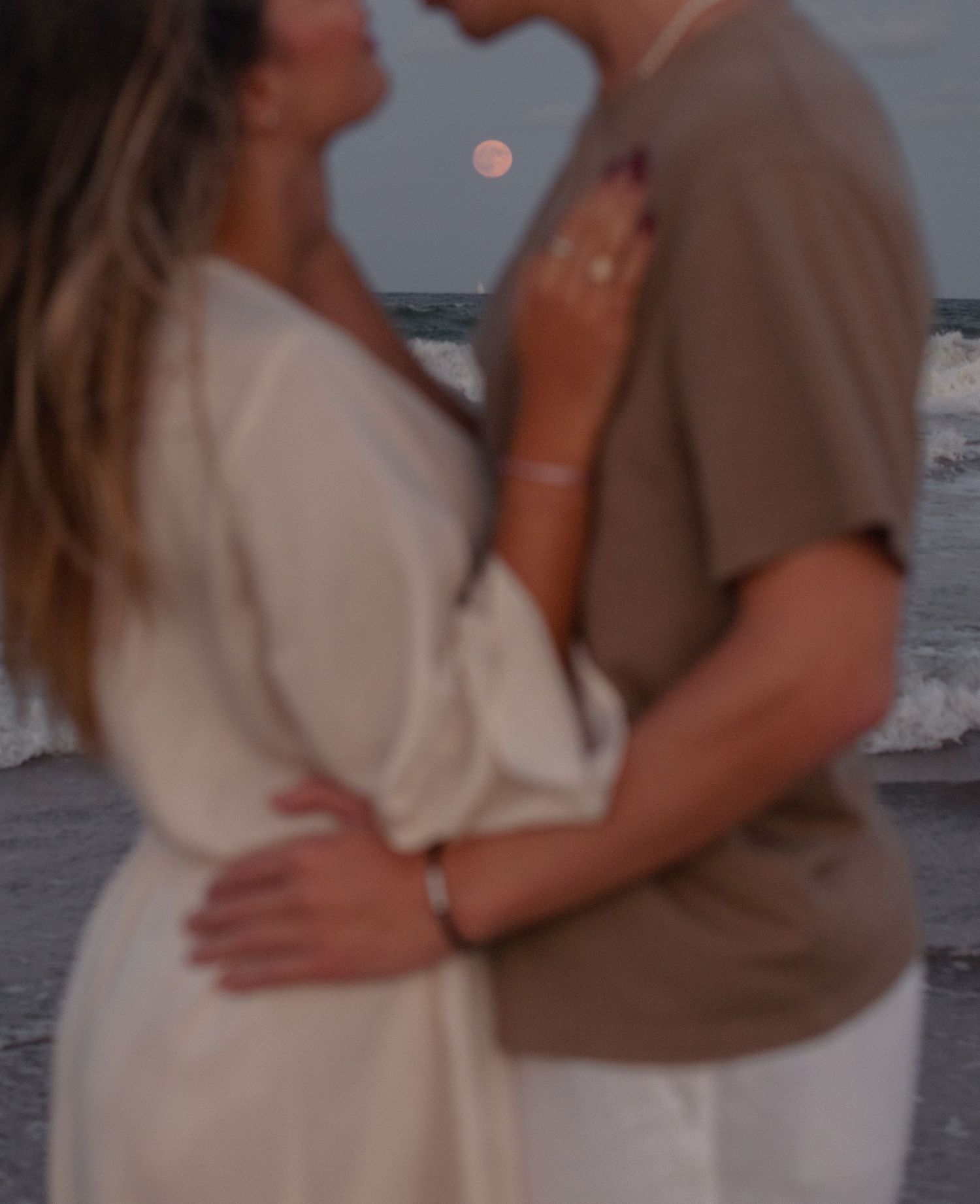 Couple embracing on beach with waves crashing behind them at dusk.