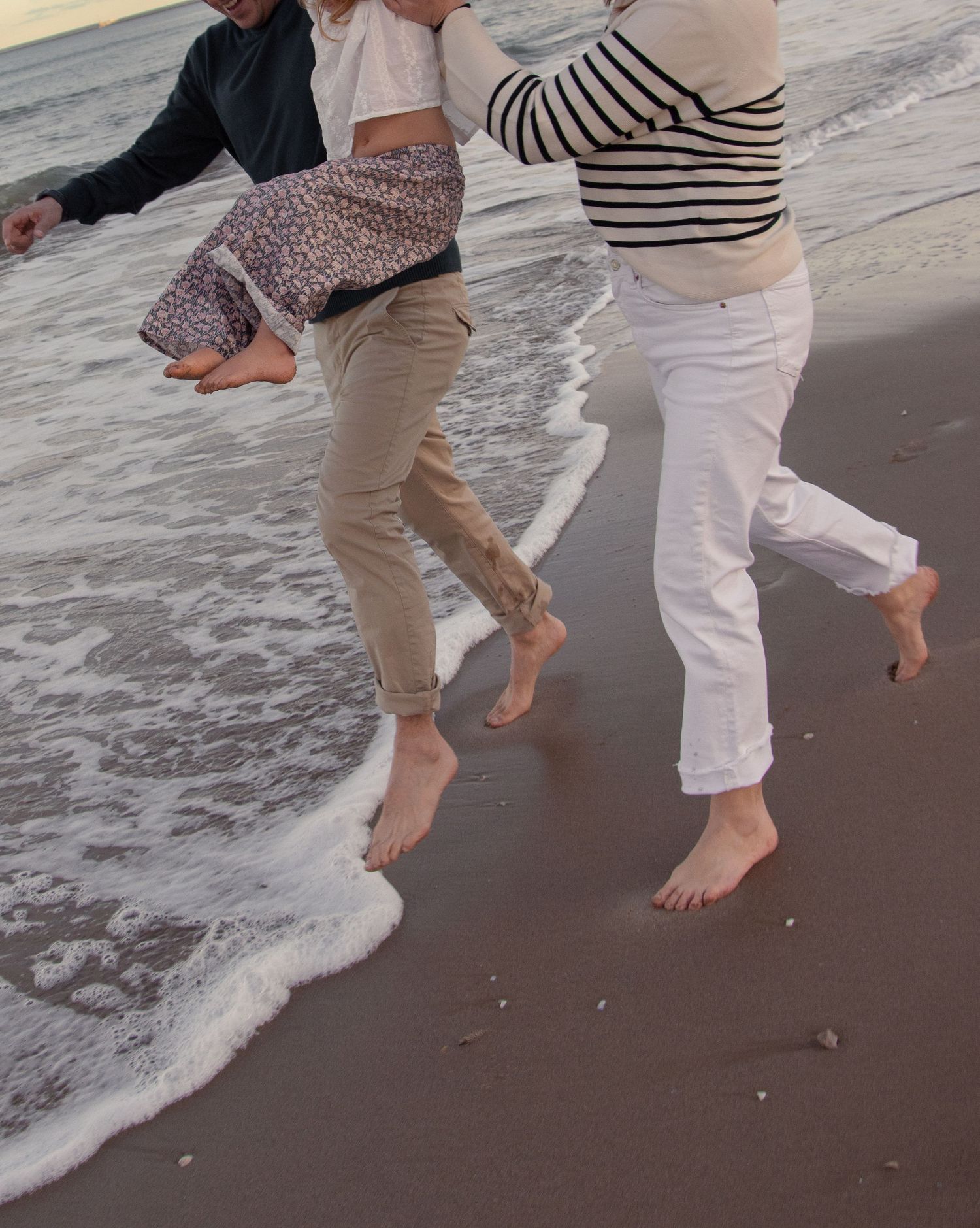 Bare feet walking along shoreline as waves wash over sandy beach.