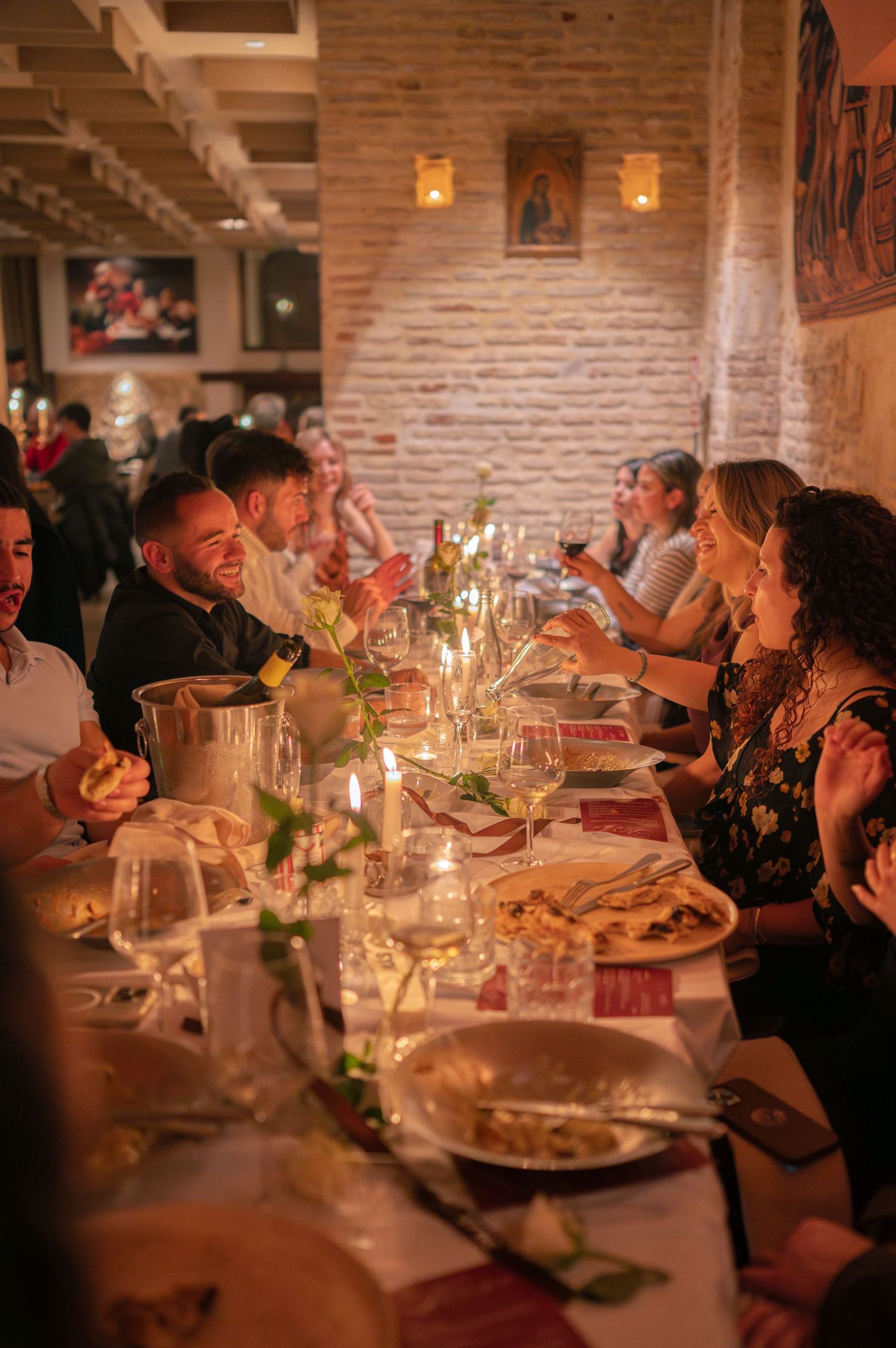 A lively dinner party scene in a restaurant with exposed brick walls and warm lighting.