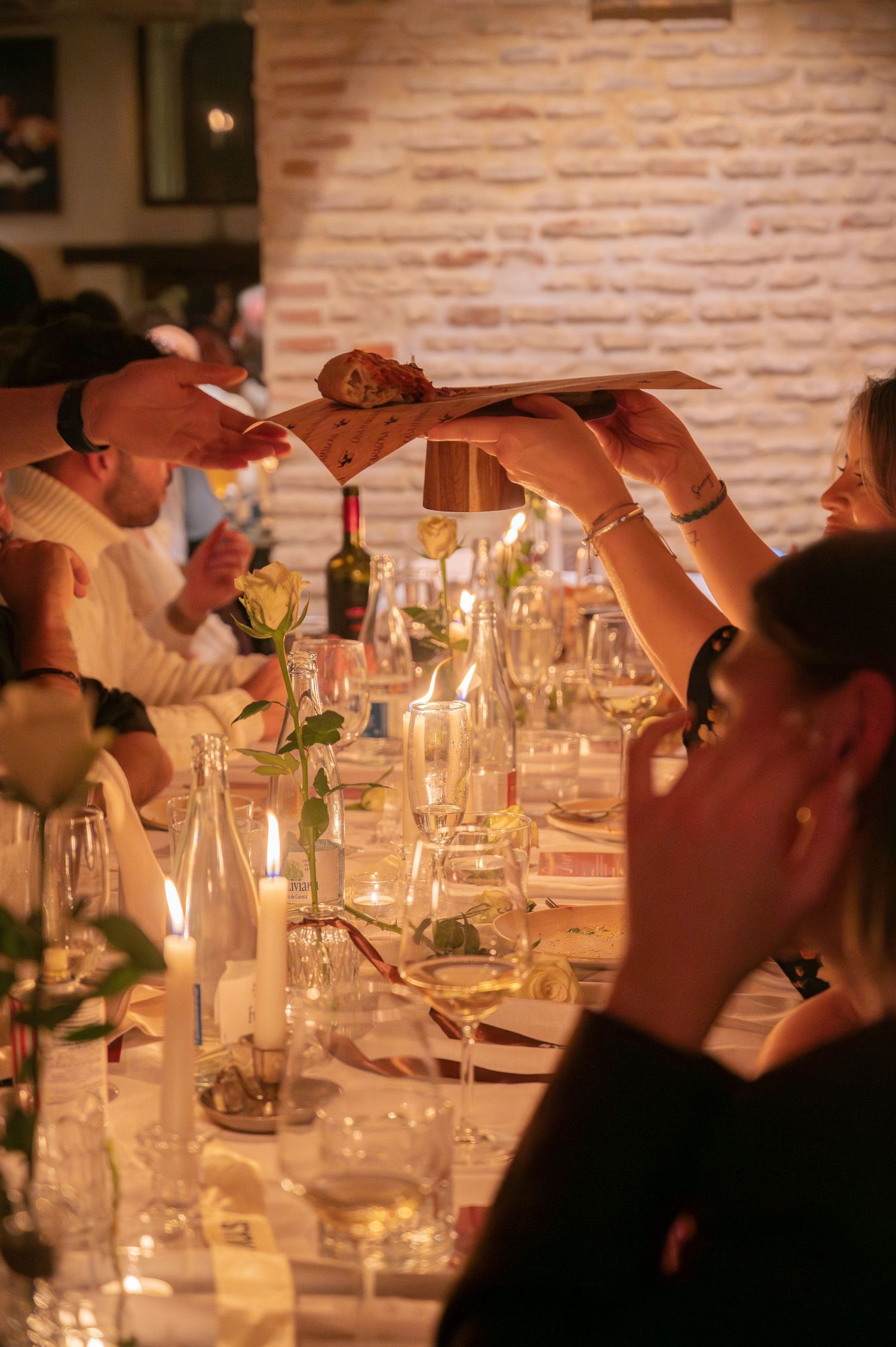 Diners sharing food across a candlelit table with wine glasses and warm lighting.