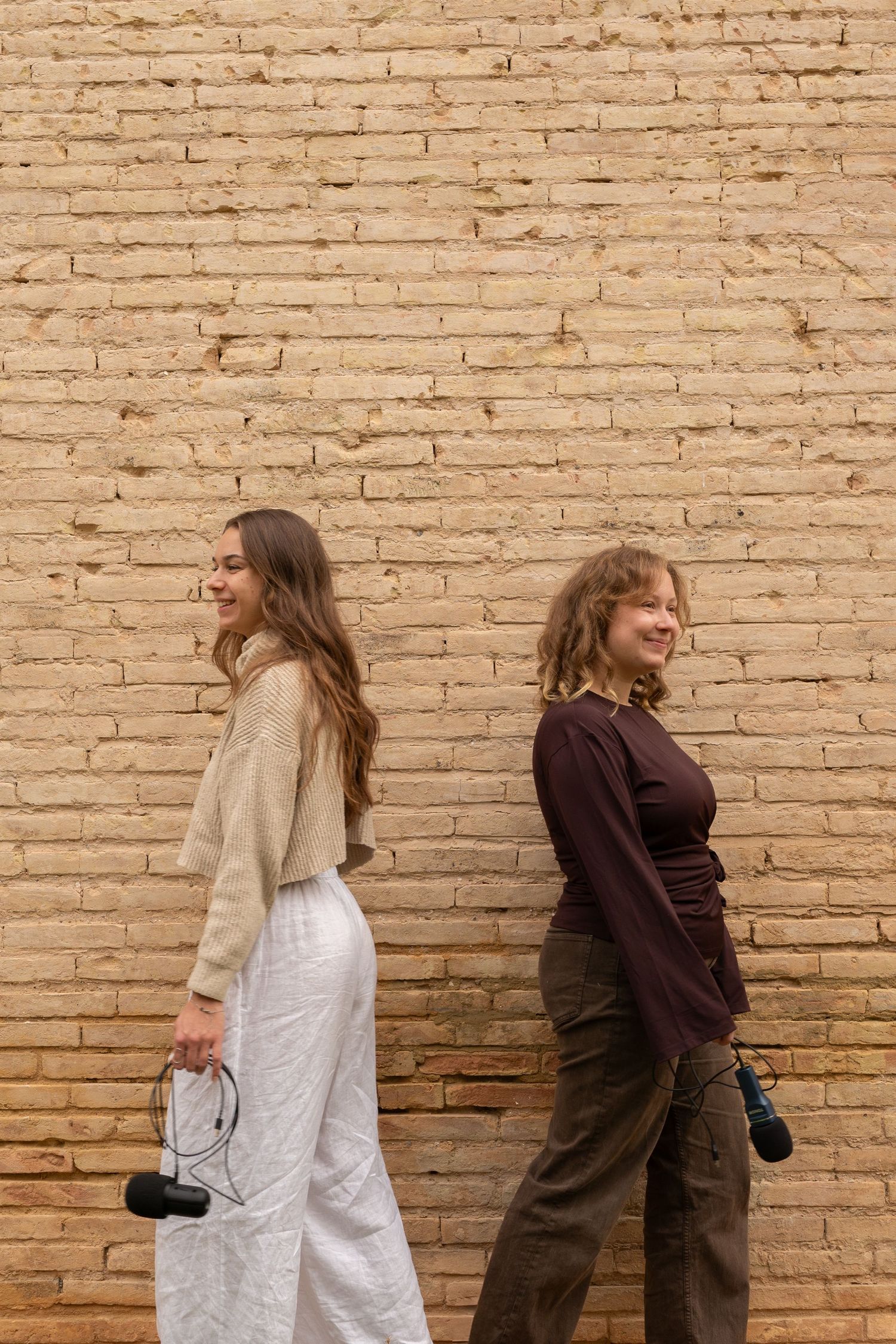 Two people in contrasting outfits interacting playfully by brick wall.