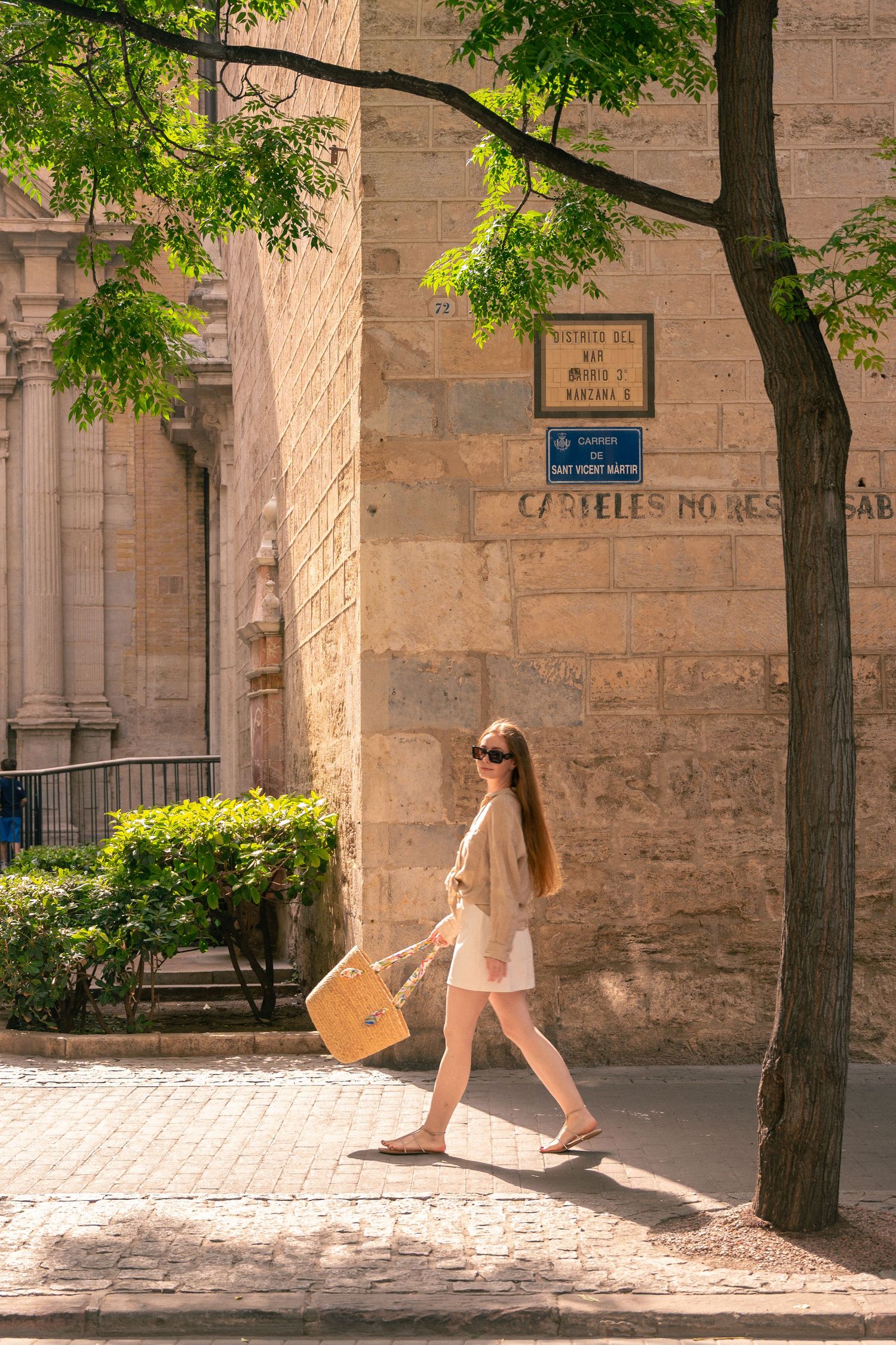 A sequence of someone walking through a sunlit stone courtyard with shopping bags.
