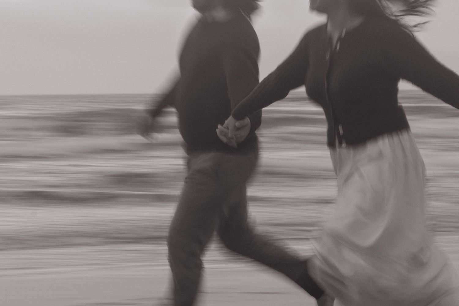 Blurred black and white image of couple running together on beach.