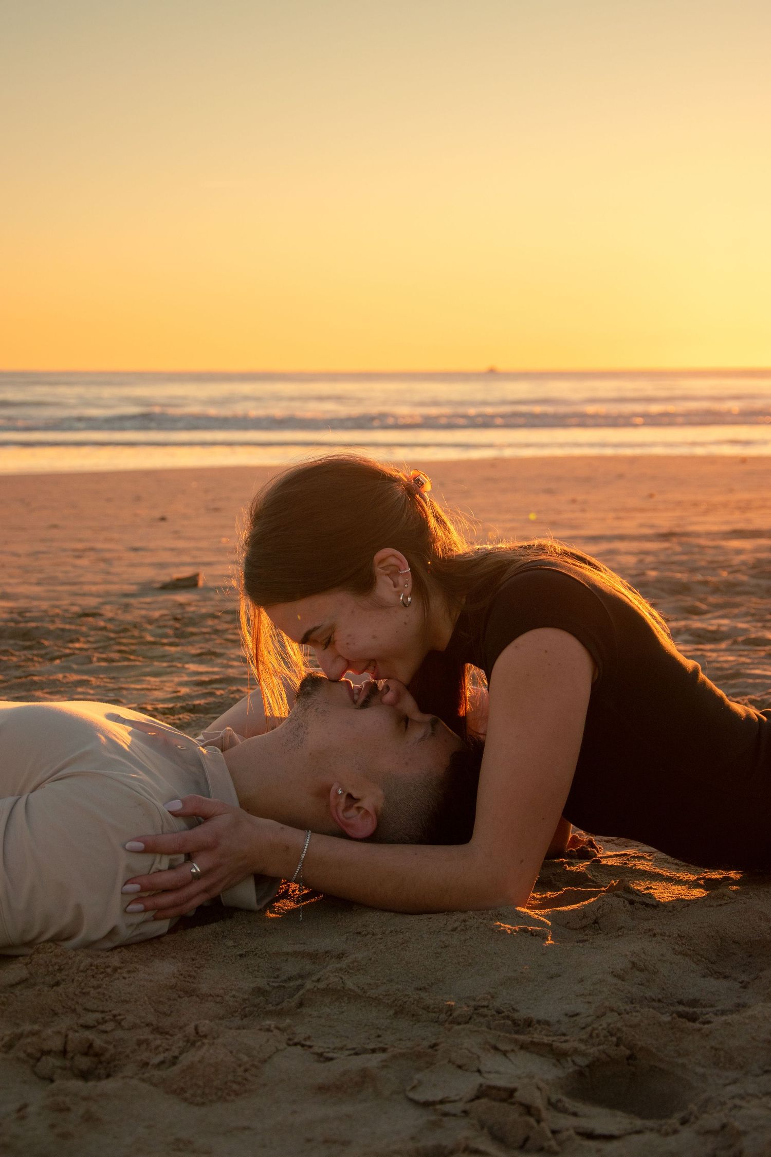Couple lying on sandy beach at golden hour sharing an intimate moment.