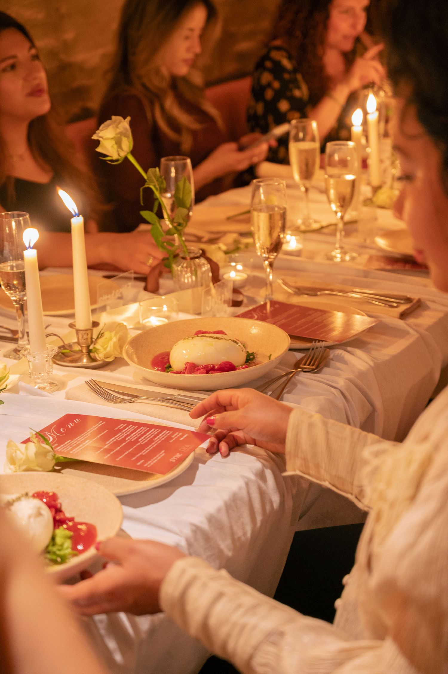 Elegant dinner table setting with candles, roses, and formal place settings in warm lighting.