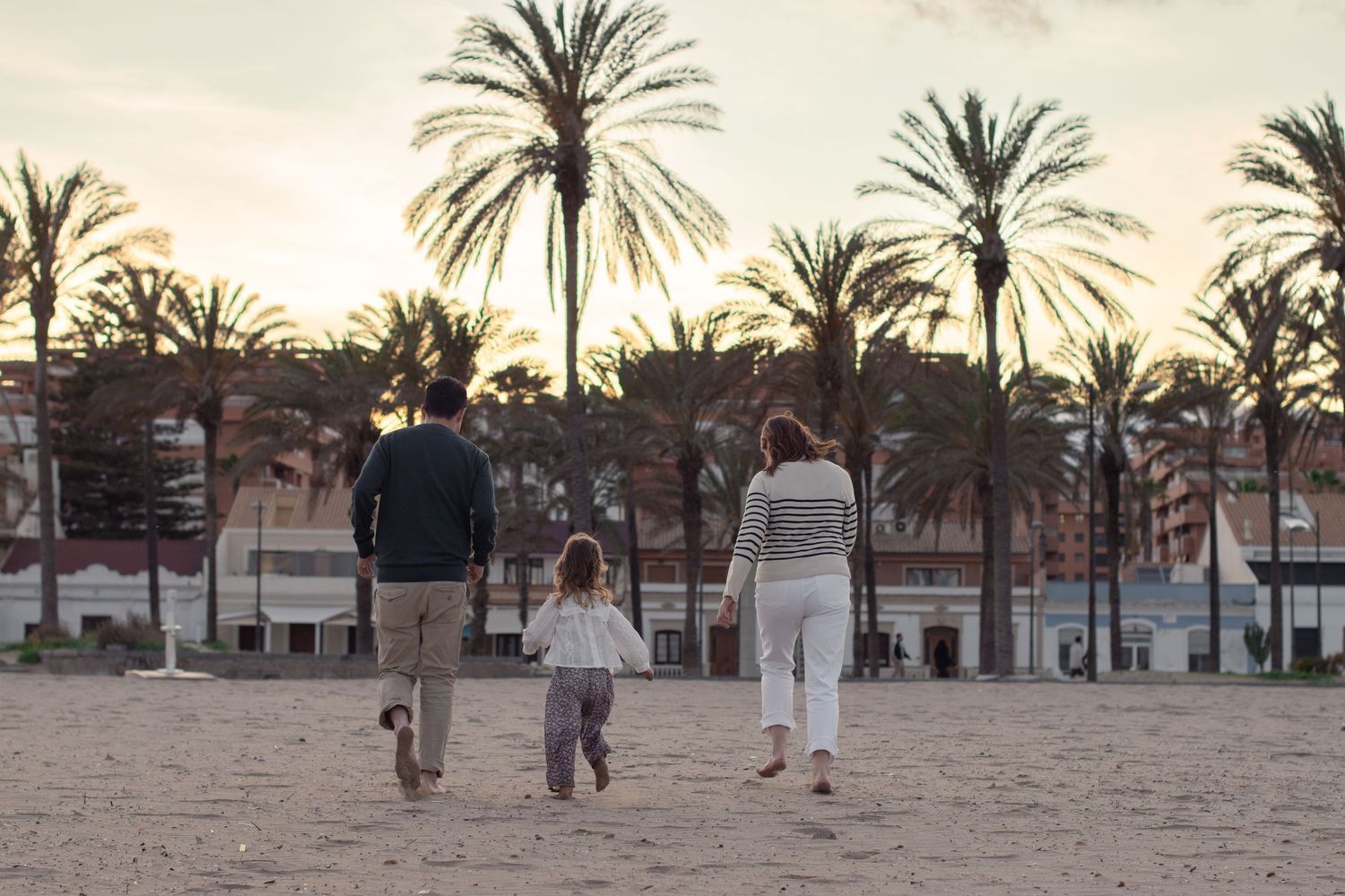 A family walks together on a beach with palm trees silhouetted against the sunset.