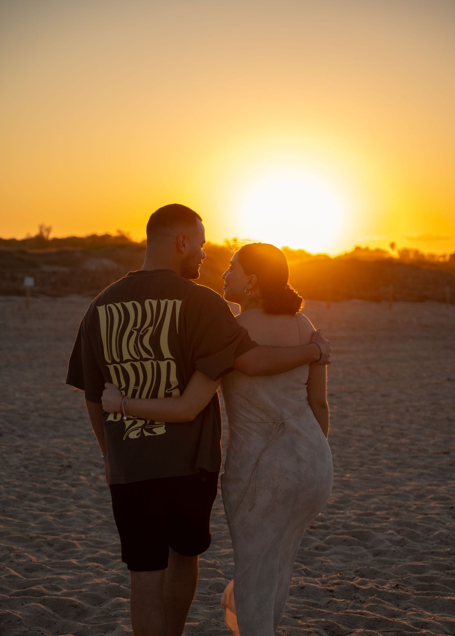 Silhouettes walking together on beach against vibrant orange sunset.