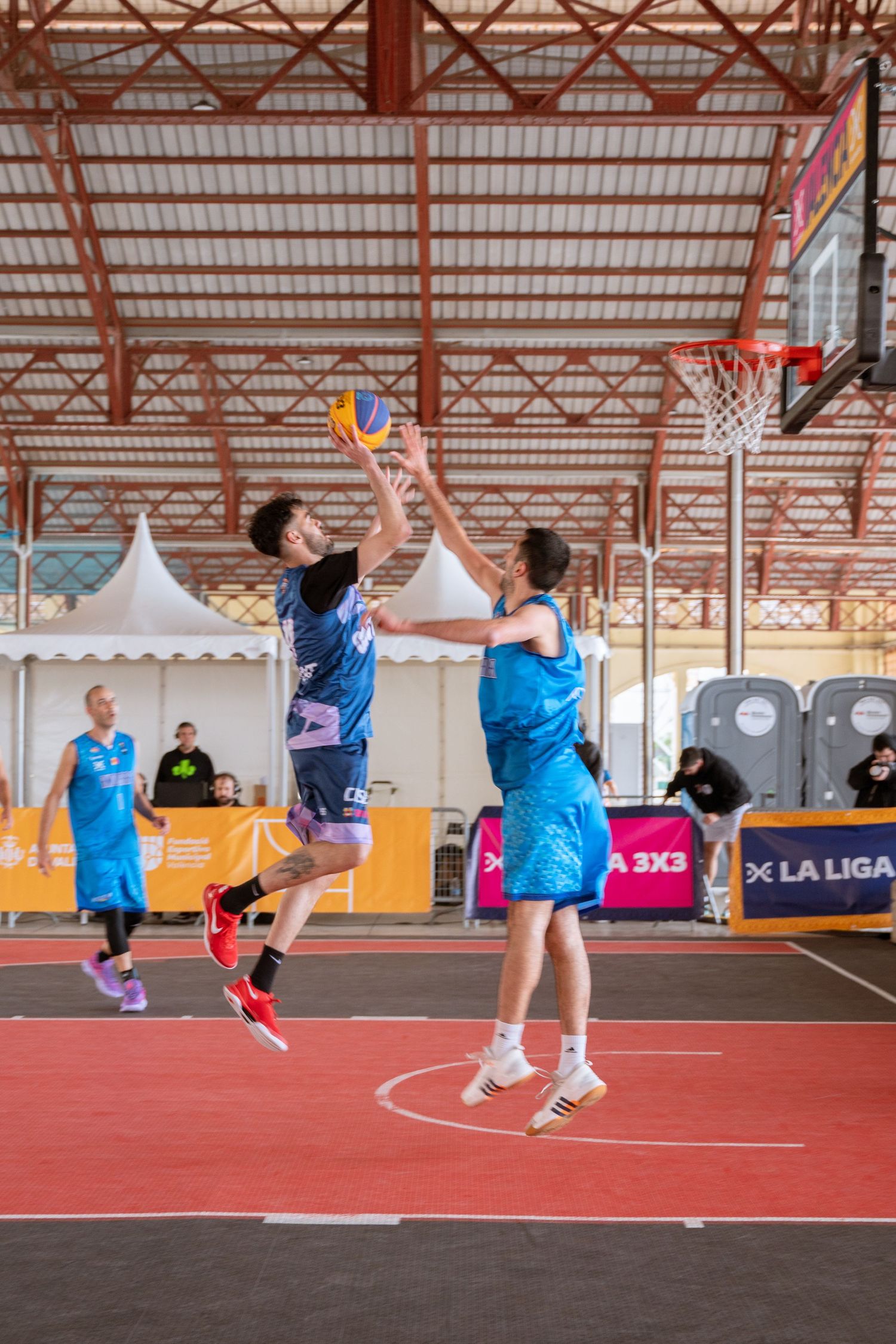 Players competing in a 3x3 basketball game under a covered outdoor court.