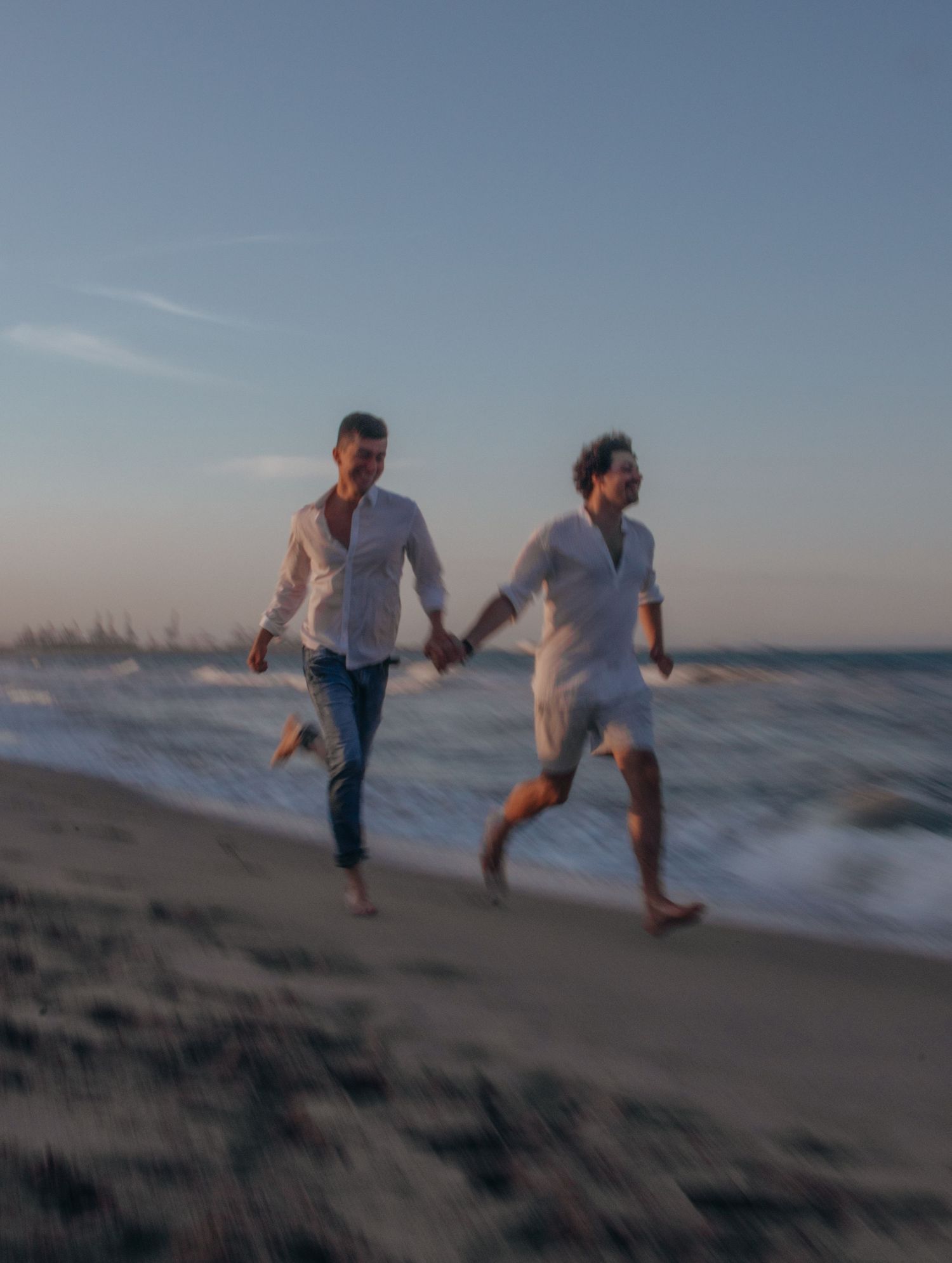 People playing and running along the beach shoreline at dusk.