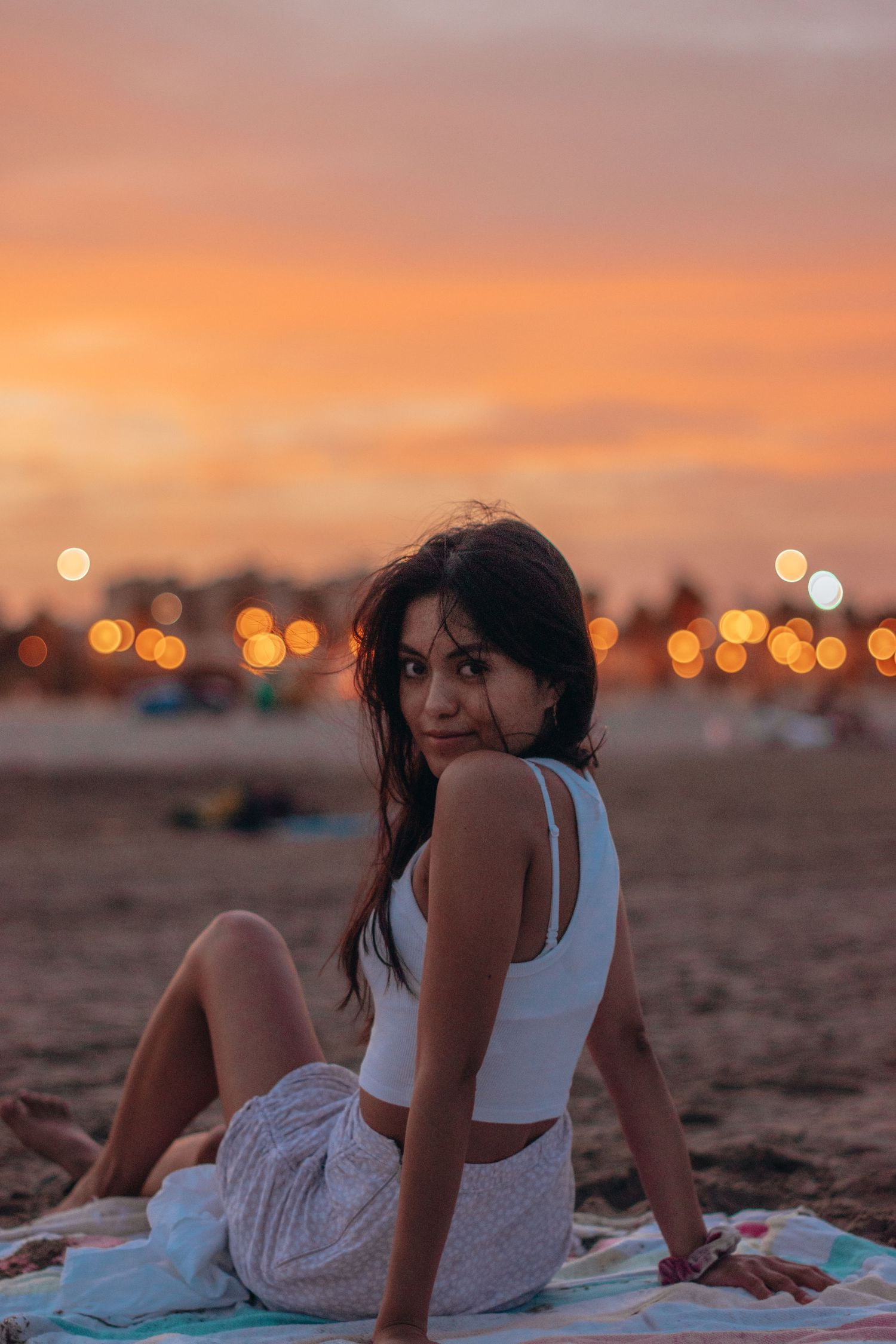 Woman relaxes on blanket at beach during golden hour sunset.
