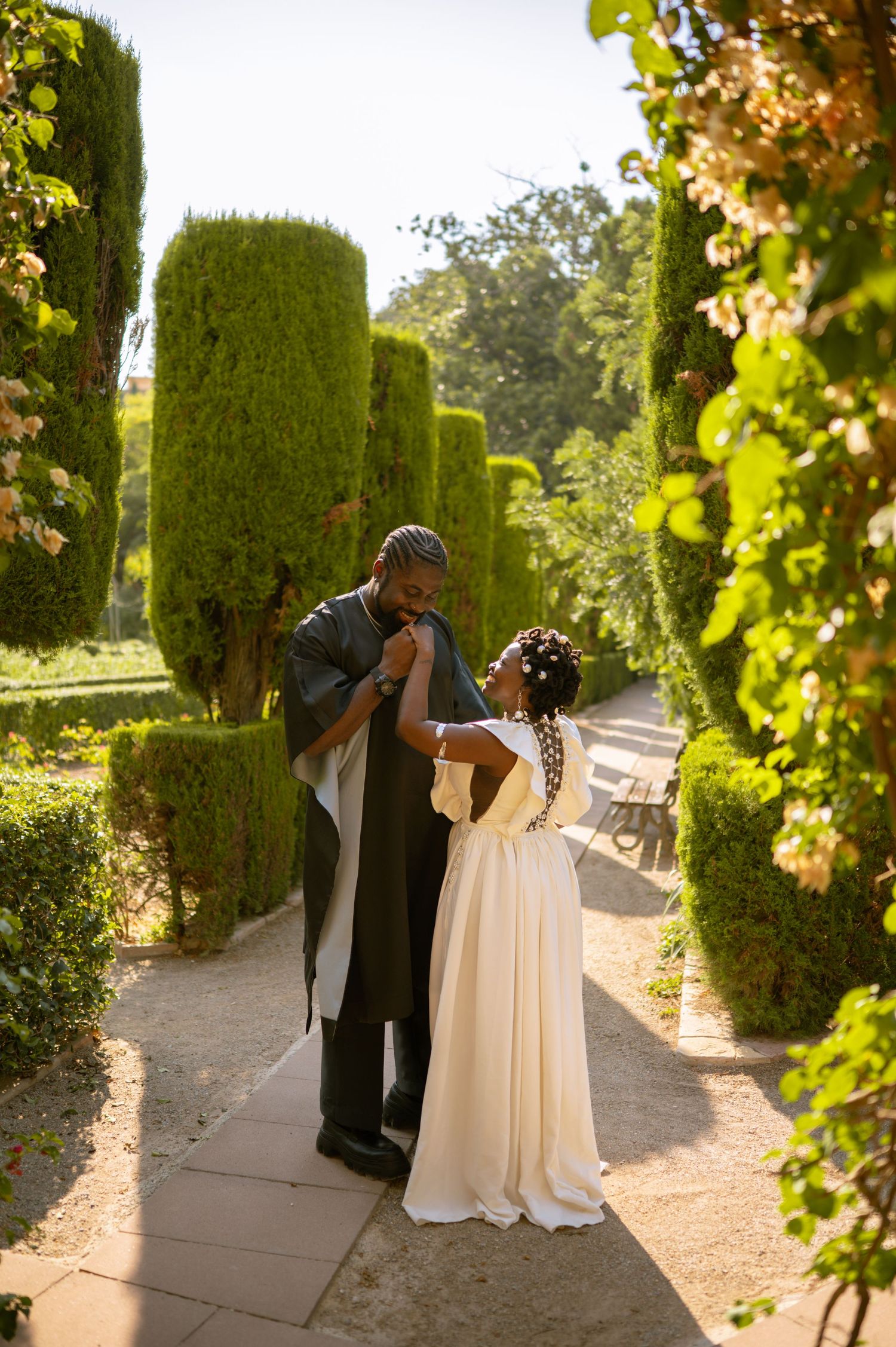 Romantic couple sharing tender moment along garden path with tall cypress trees.