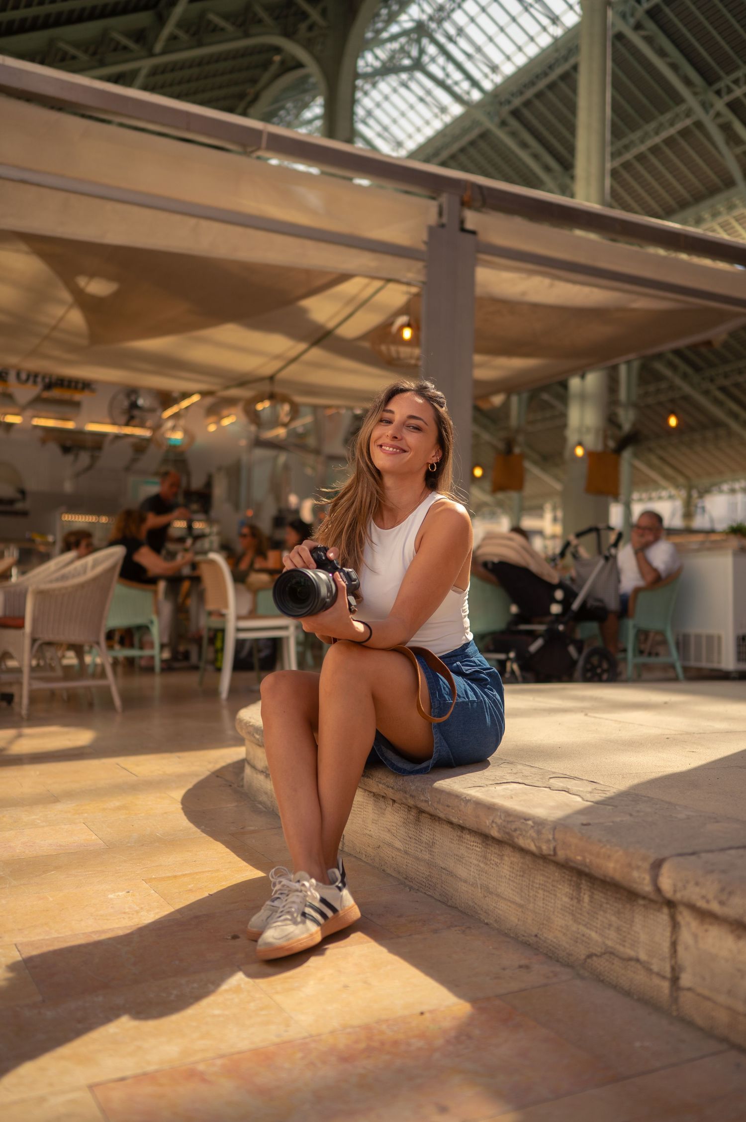 A person sitting on a stone ledge in a bright indoor space with glass ceiling and ambient lighting.