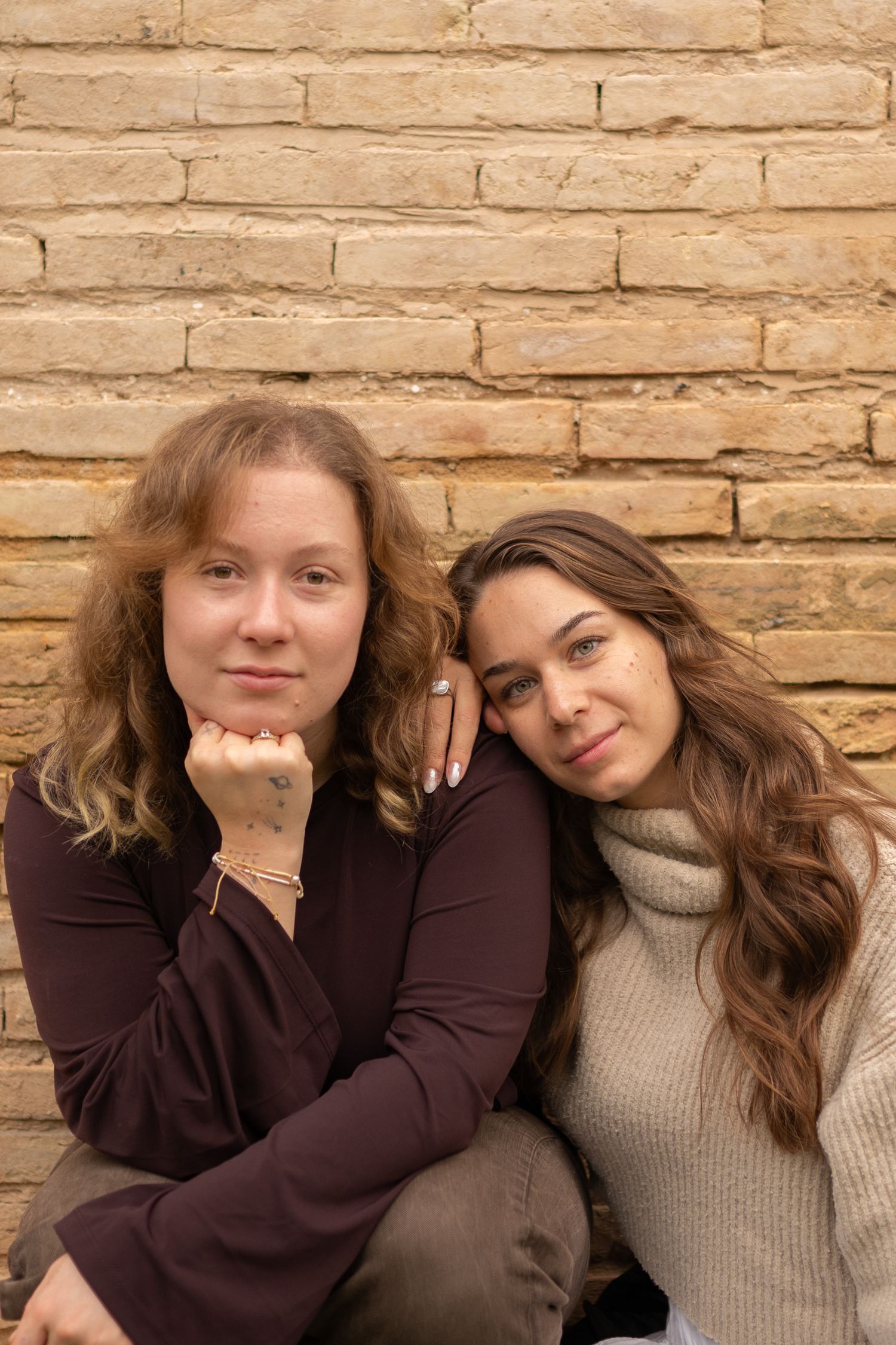 Two people in casual wear posing against brick wall background.