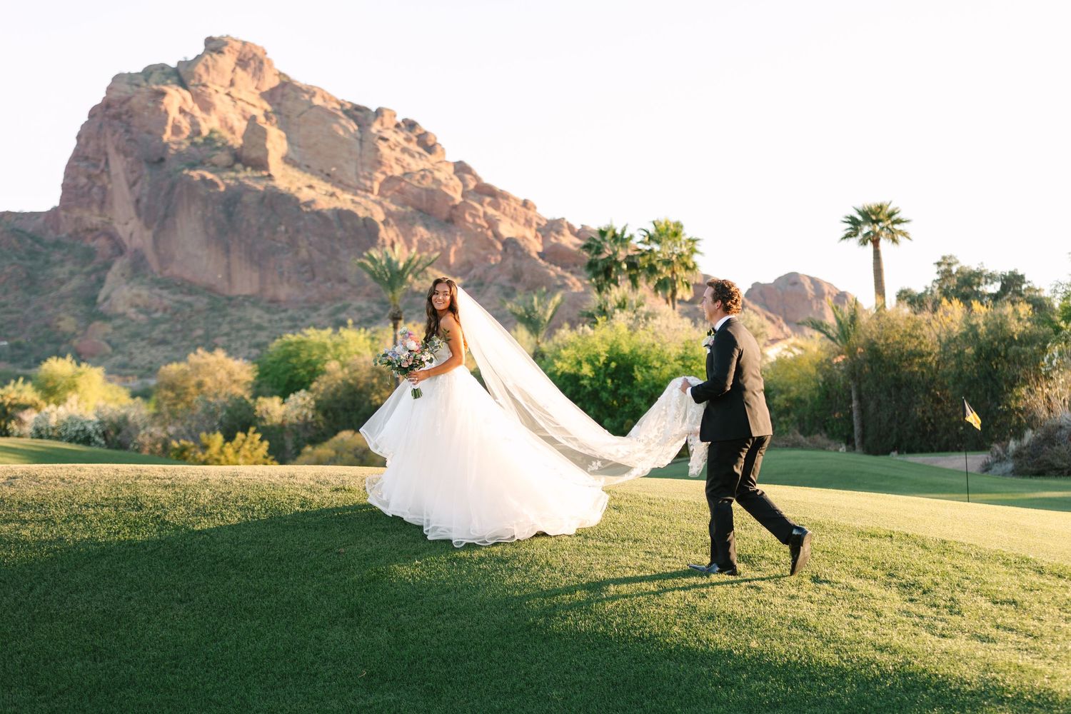 Wedding couple walking on manicured lawn with dramatic mountain landscape.