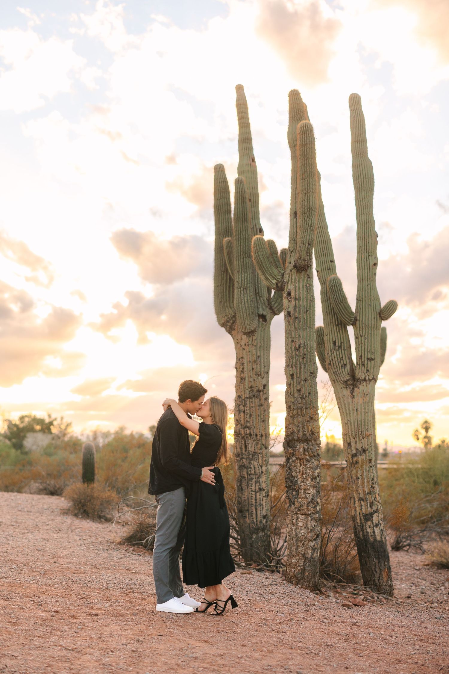 A couple shares an intimate moment at sunset among tall saguaro cacti in the Arizona desert landscape.