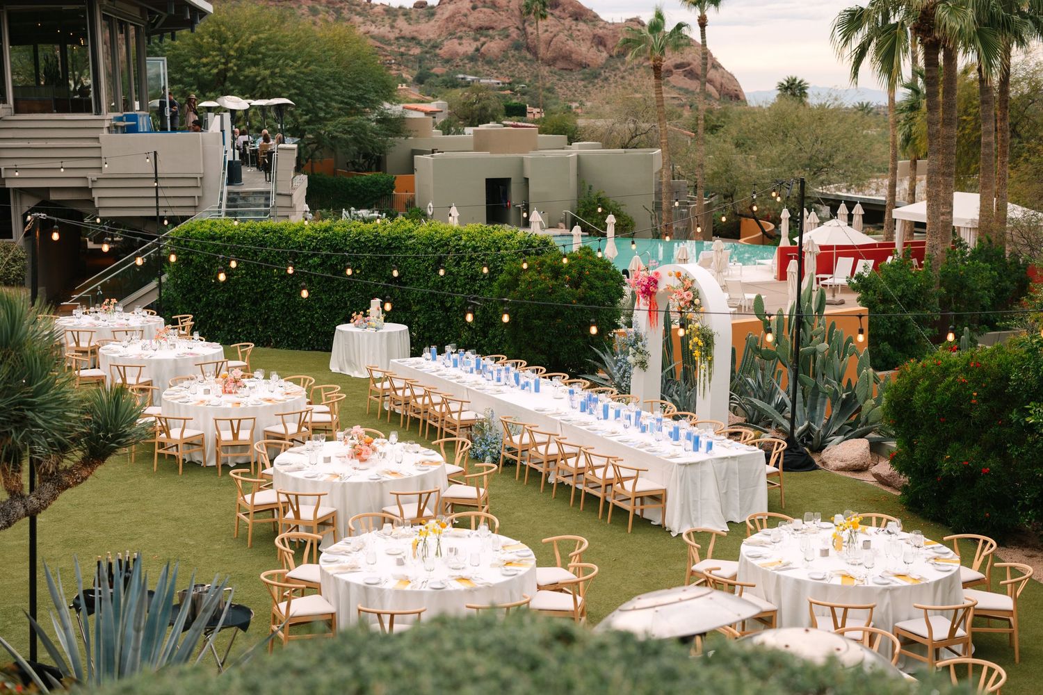 Elegant outdoor wedding reception setup with round tables and string lights in a garden setting with mountain views.