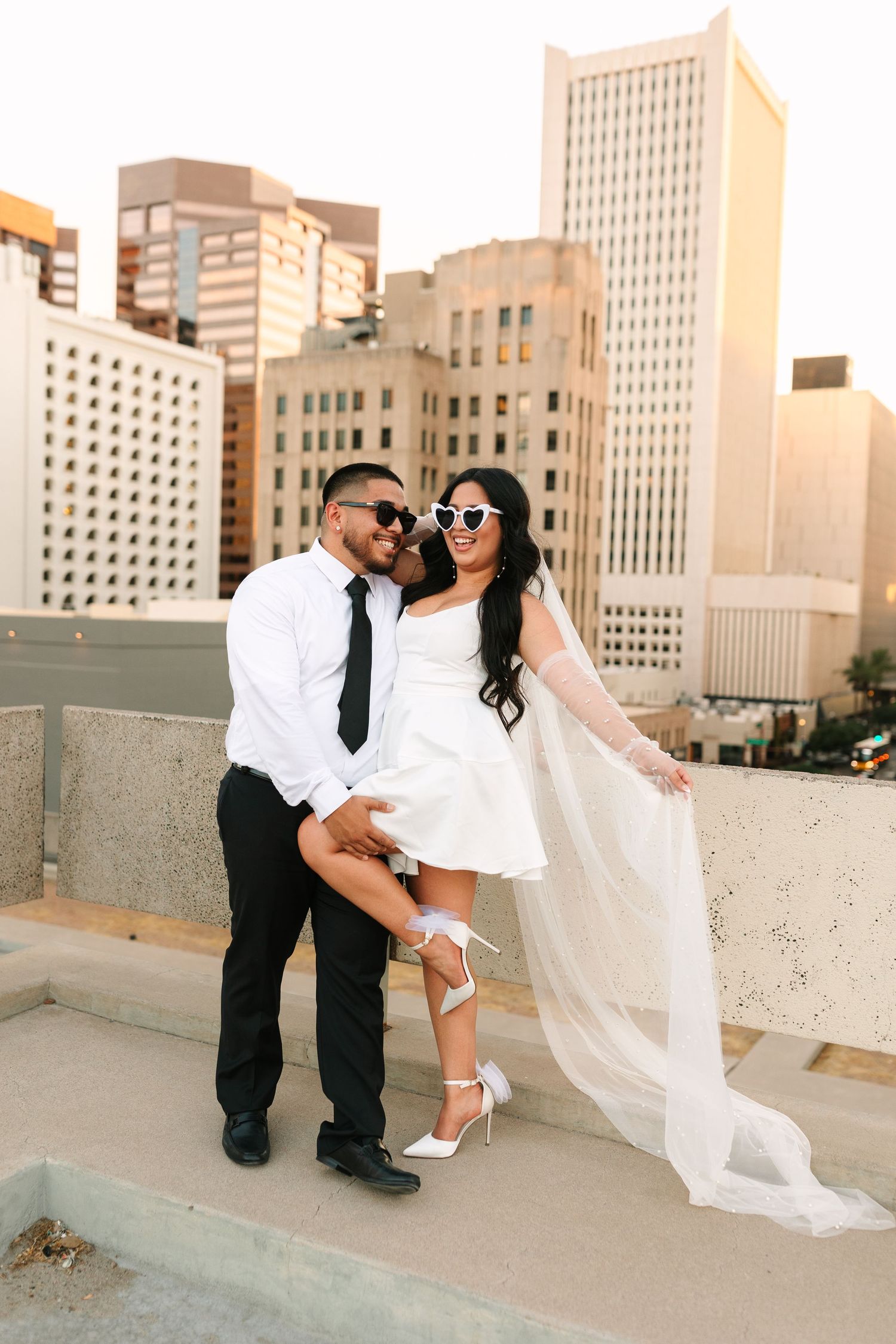 Romantic urban rooftop photoshoot sequence with couple in white and black attire against city skyline at sunset.