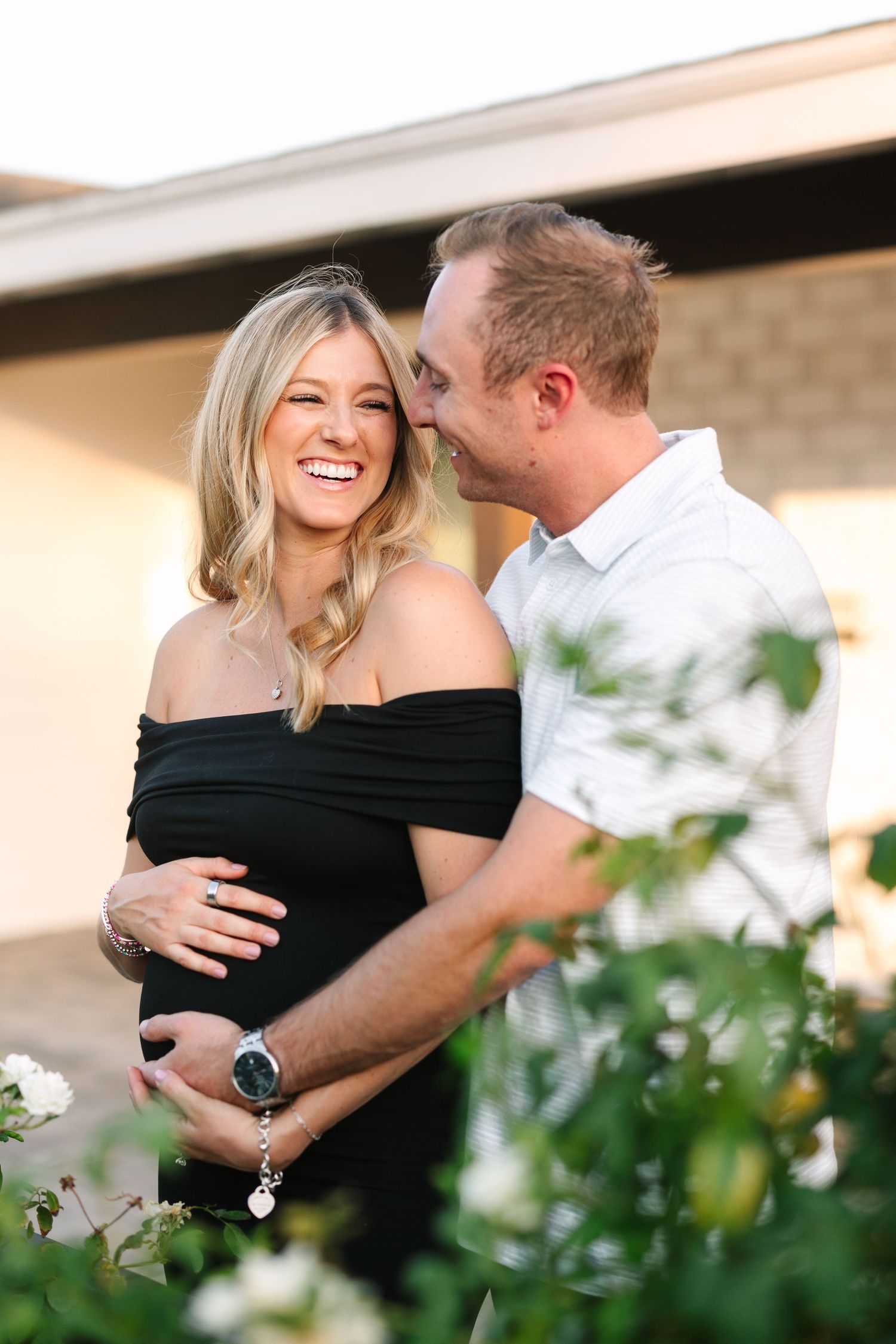 A romantic outdoor couple wearing black and white share an intimate moment while smiling among greenery.