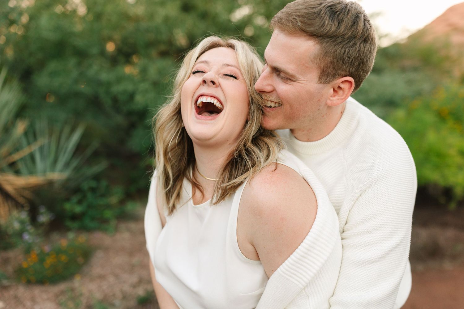 A couple shares a joyful moment together while embracing outdoors in a garden setting.