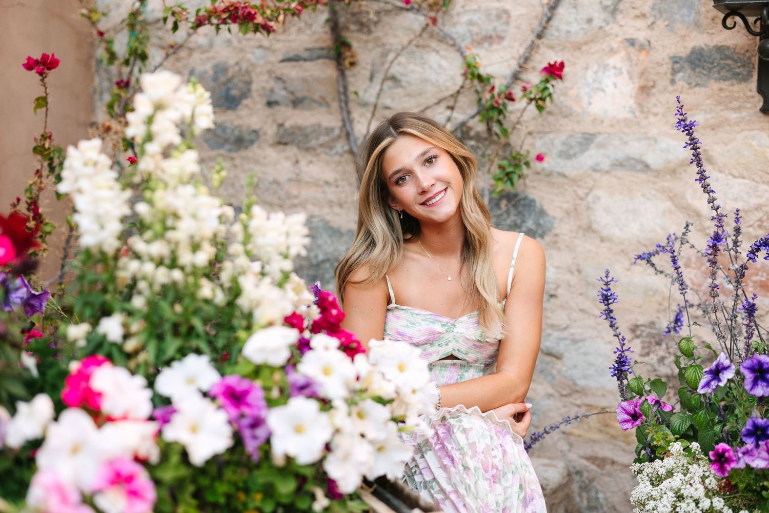 Beautiful summer garden scene with colorful flowers including pink, white and purple blooms against rustic stone wall.