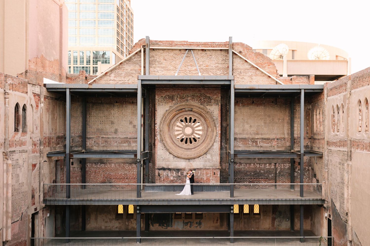 A vintage circular clock face mounted on a weathered brown industrial wall with symmetrical architectural details.