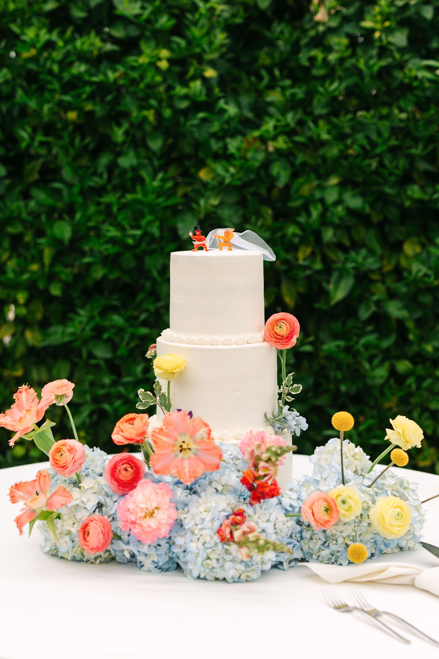 An elegant white wedding cake adorned with peach and yellow flowers against greenery.