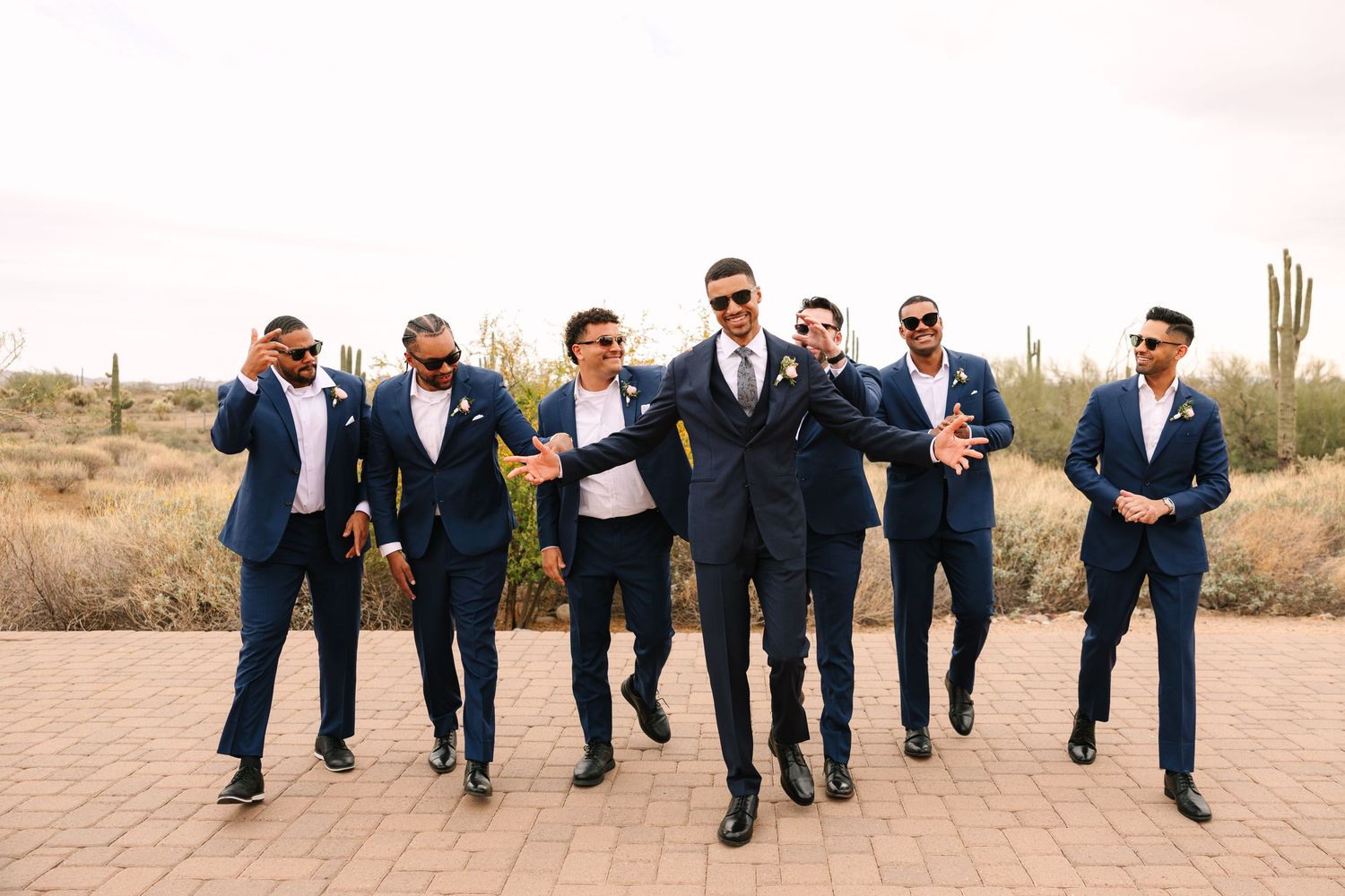 Groomsmen in navy suits walking together in desert landscape.