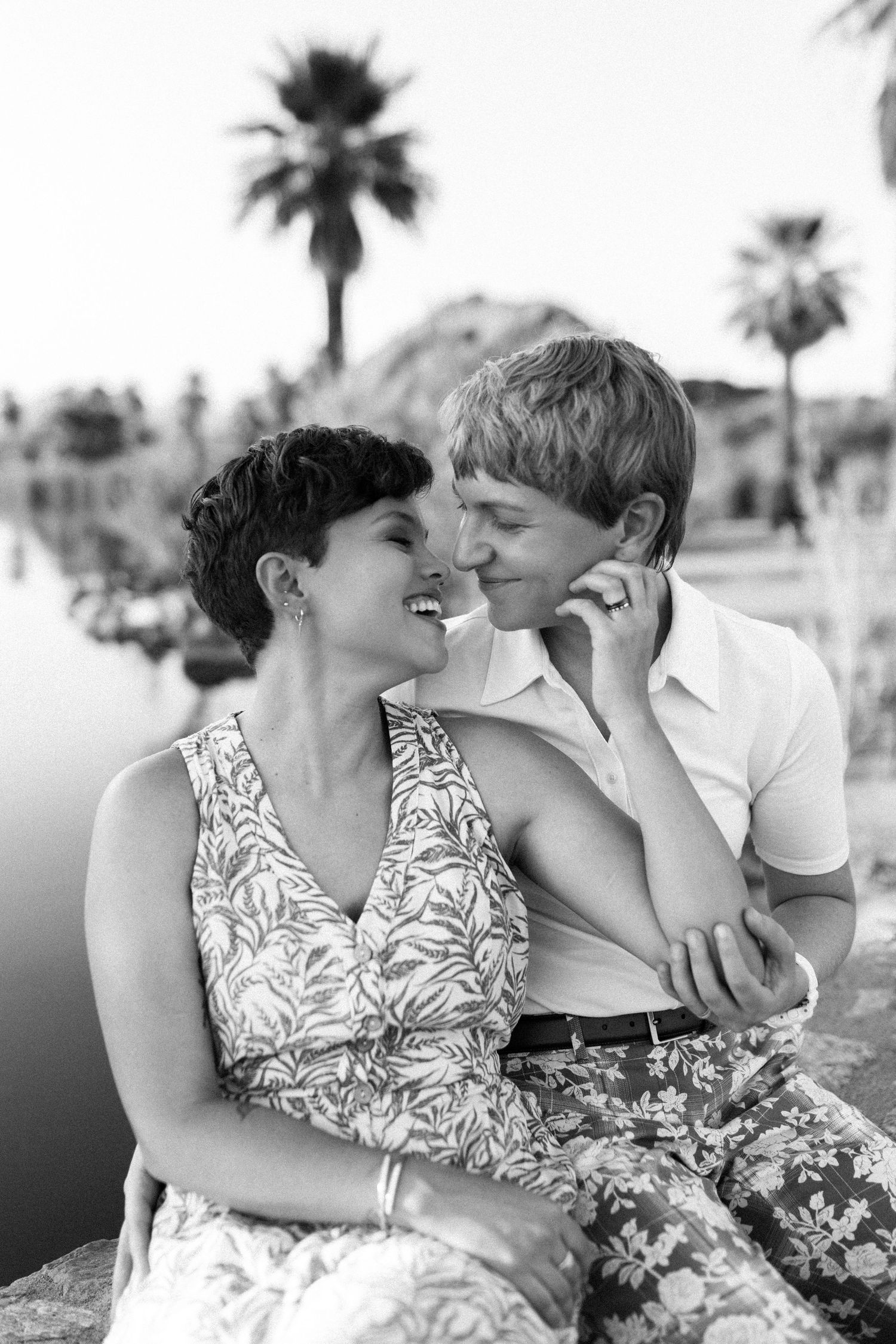 A romantic black and white portrait of a couple sharing an intimate moment with palm trees in the background.