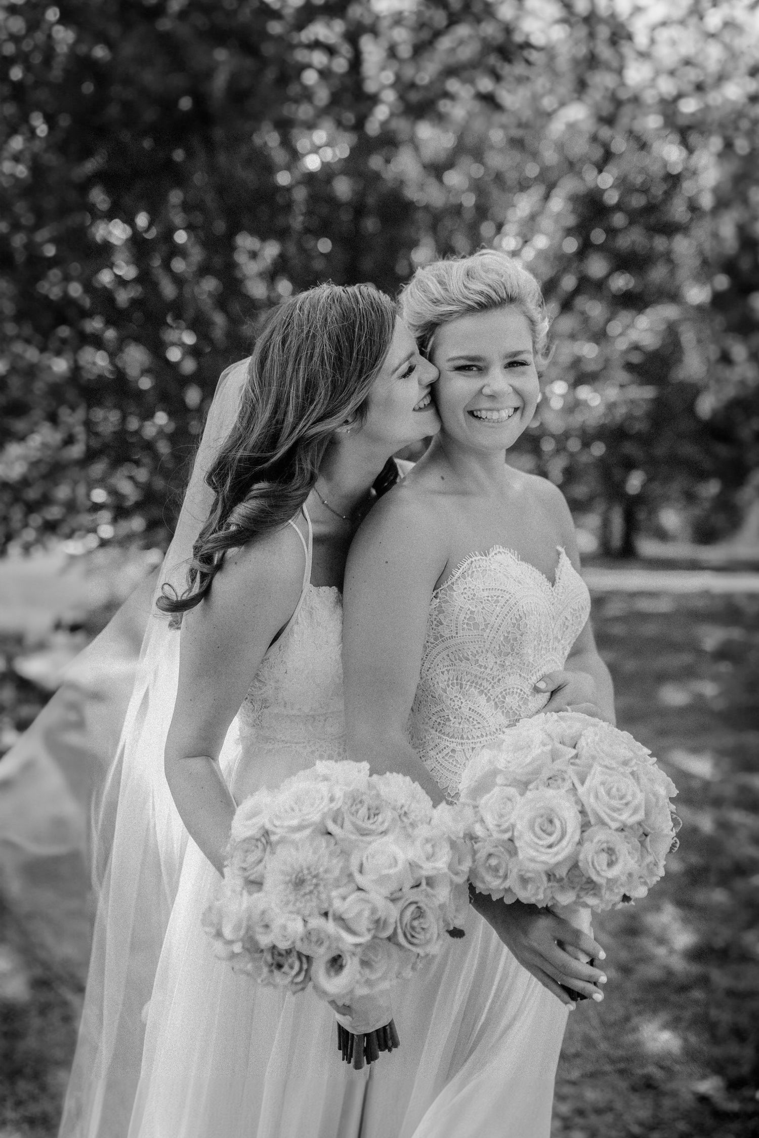 Bridesmaids in white dresses hold elegant white rose bouquets during outdoor wedding. Molly McPhoto