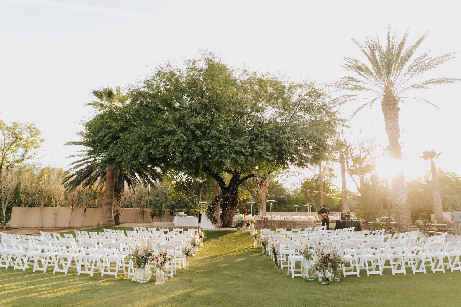 Panoramic view of outdoor wedding ceremony setup with white chairs and palm trees at sunset. Molly McPhoto