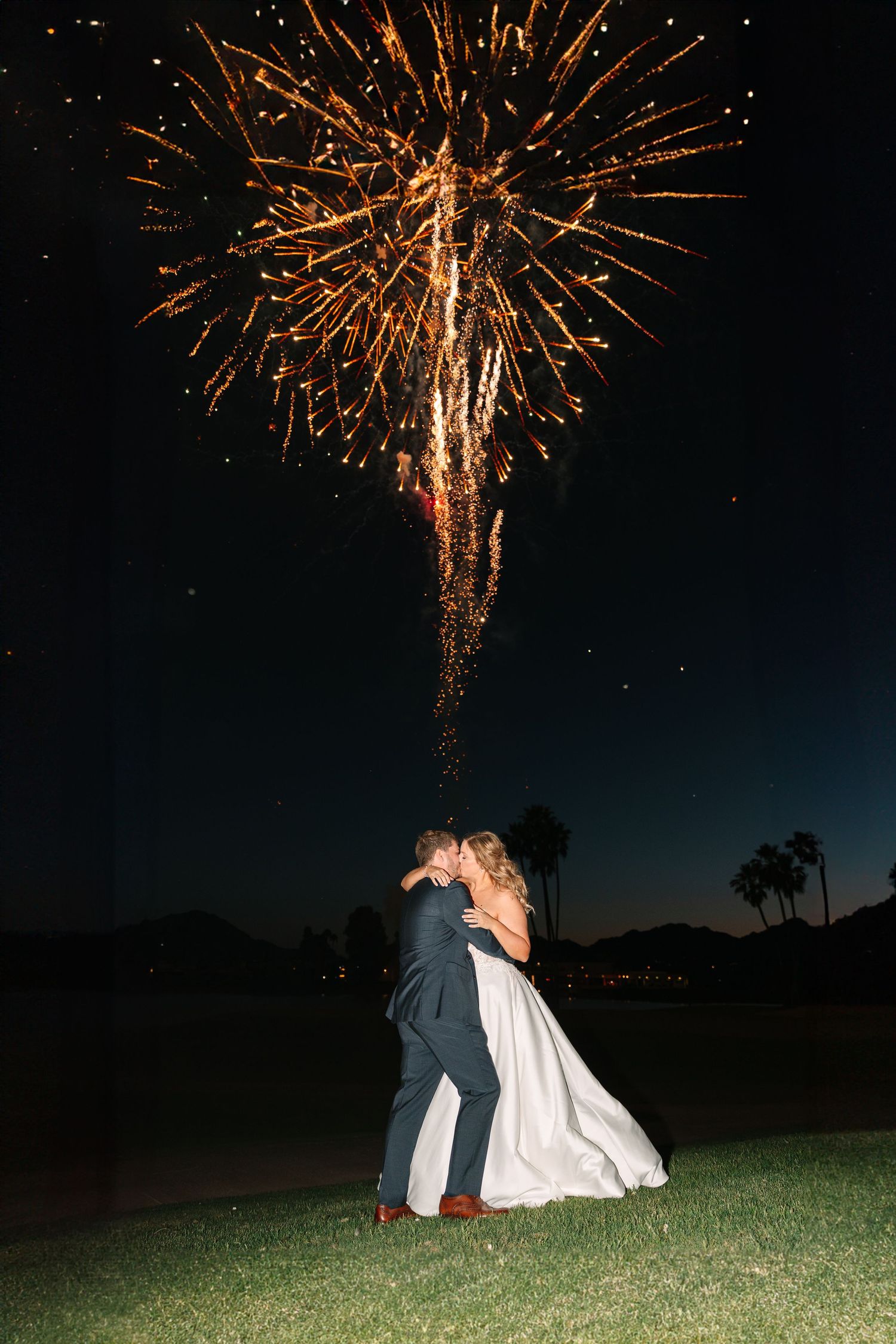 Wedding couple silhouetted against spectacular fireworks display in night sky.