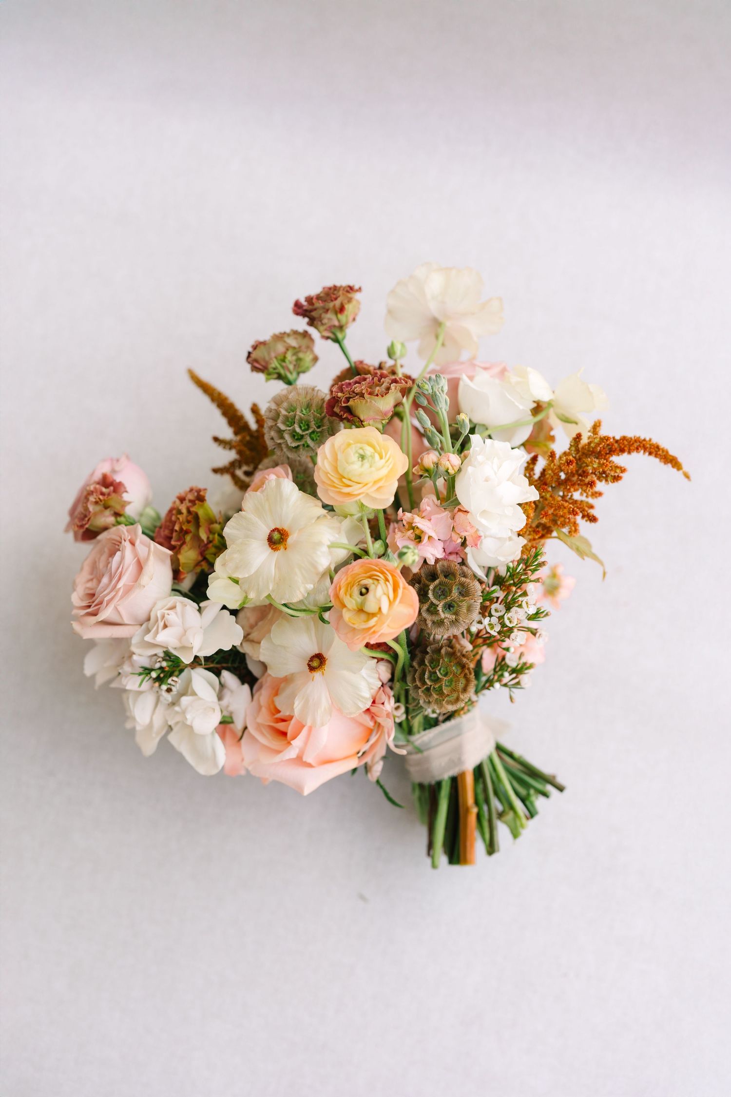 A romantic bouquet of peach and white garden roses with greenery arranged against a light background.